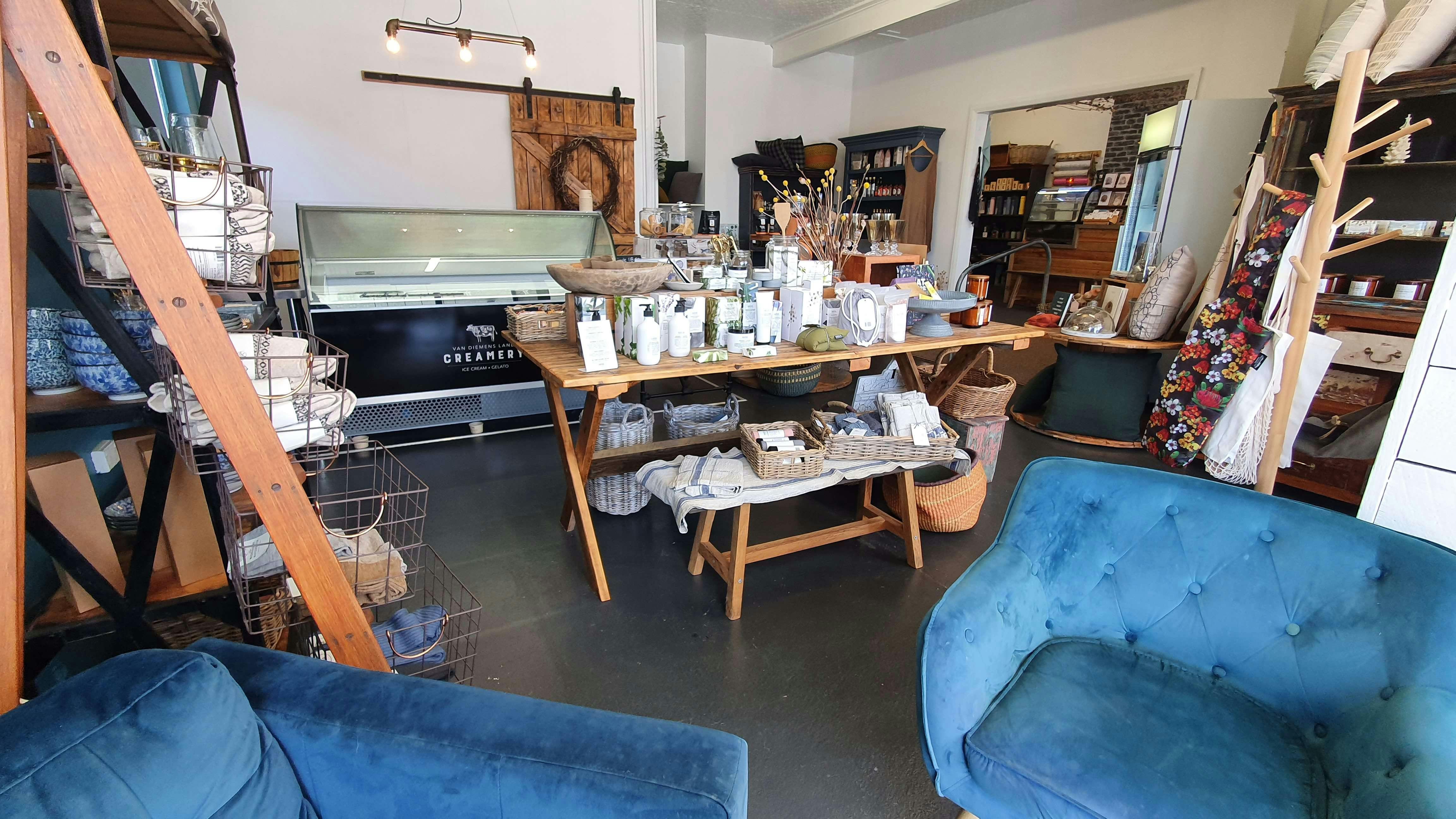 The interior of a shop, with white walls, blue chairs, a wooden table with colourful display