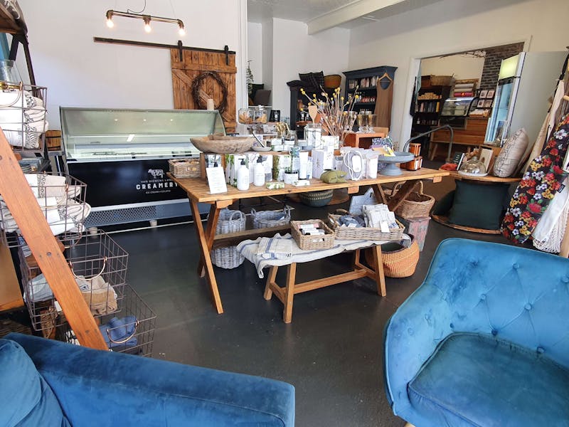 The interior of a shop, with white walls, blue chairs, a wooden table with colourful display