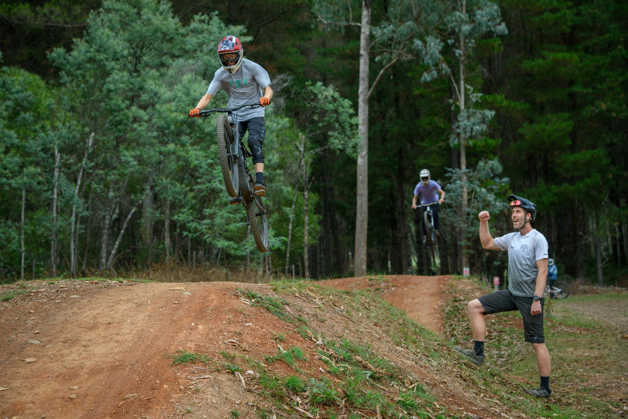 A group of riders on bikes jump into the air while a coach watches on from the ground.