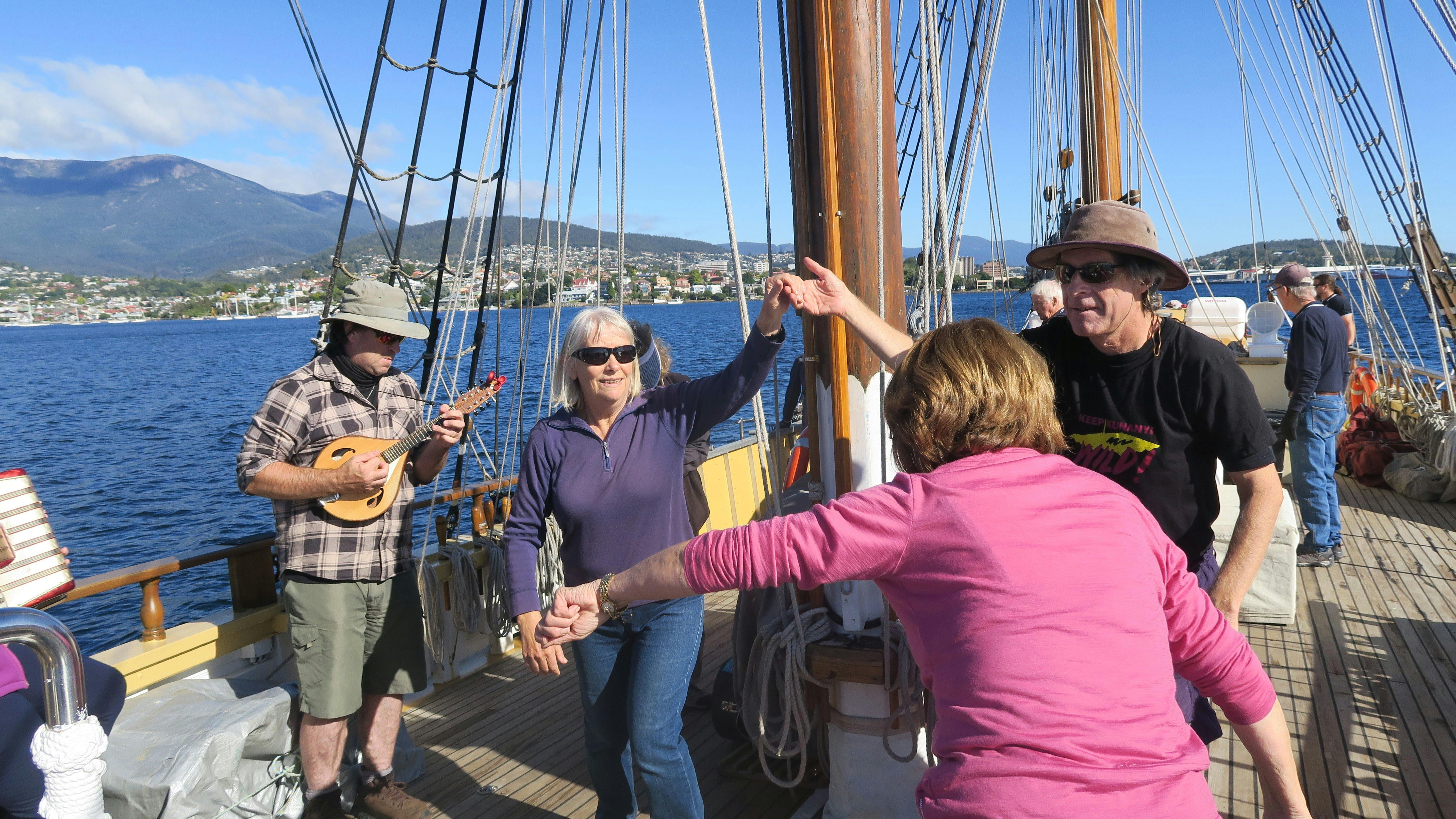 small groups dancing on the deck of the Lady Nelson, whilst a man plays a ukulele
