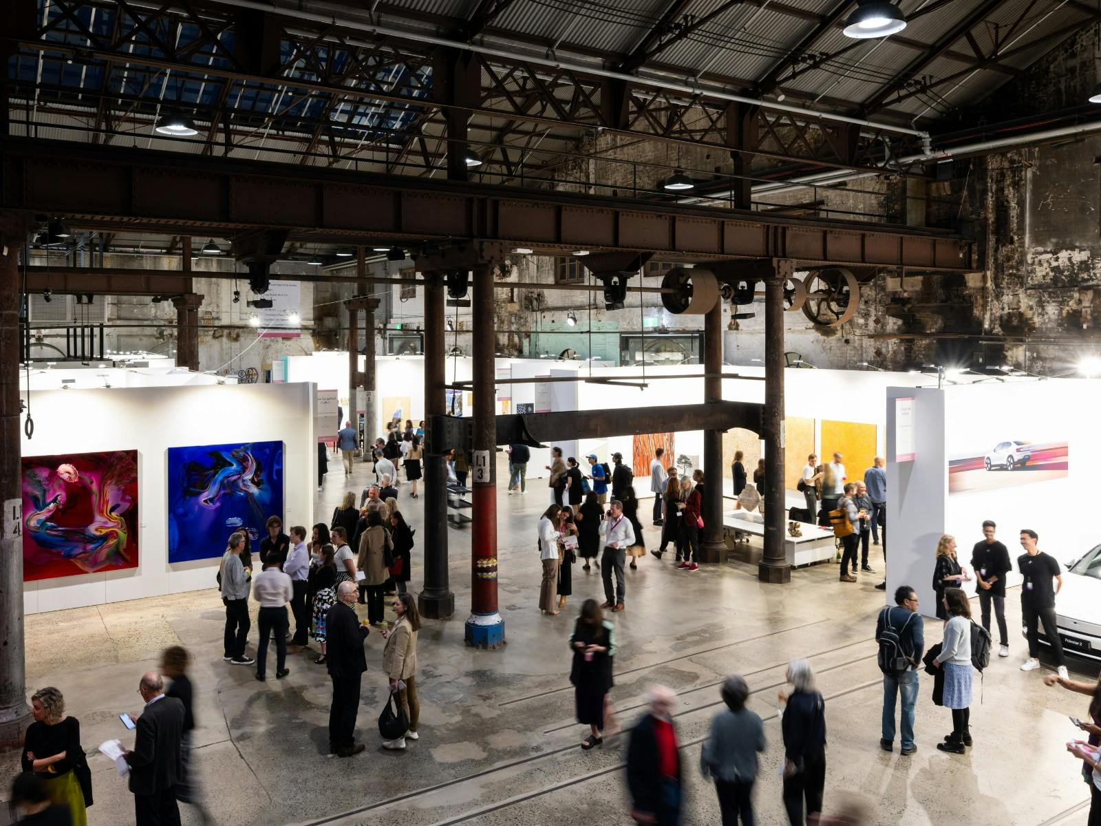 広々とした屋内アートフェアで、人々が歩きながらアート作品を鑑賞しています。