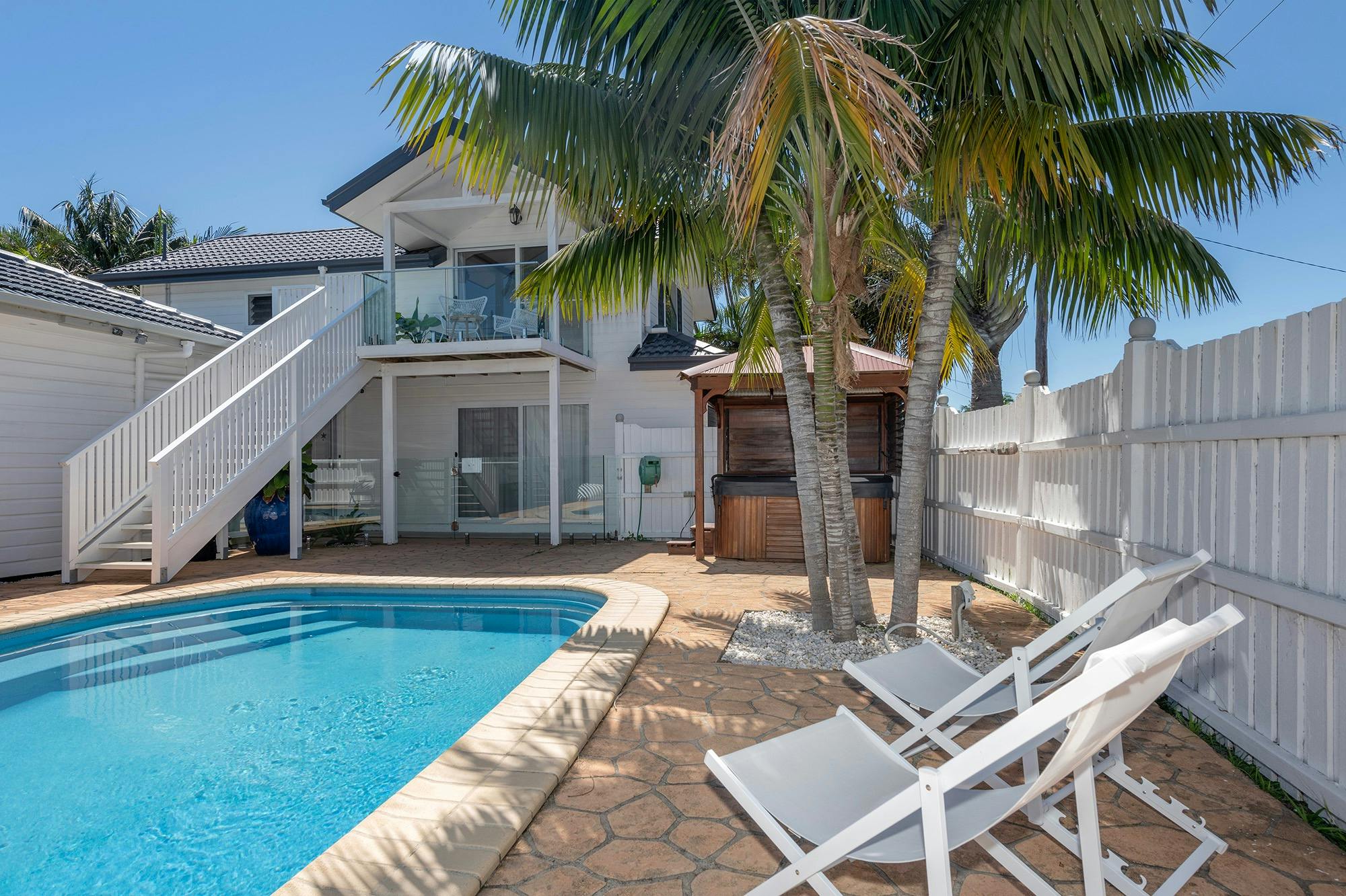 大きなアクアブルーの埋め込み式プール、デッキチェア、地上の杉板張りのスパを備えたプールエリア