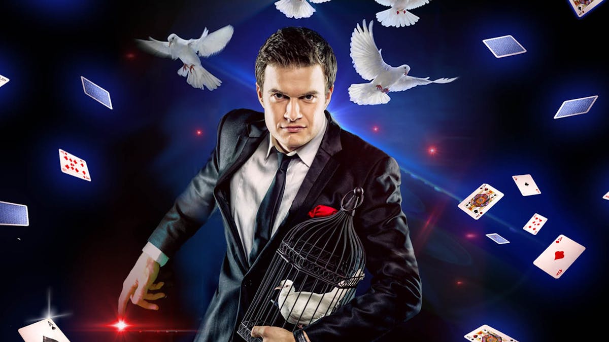 Magician holding birdcage as doves and playing cards float around
