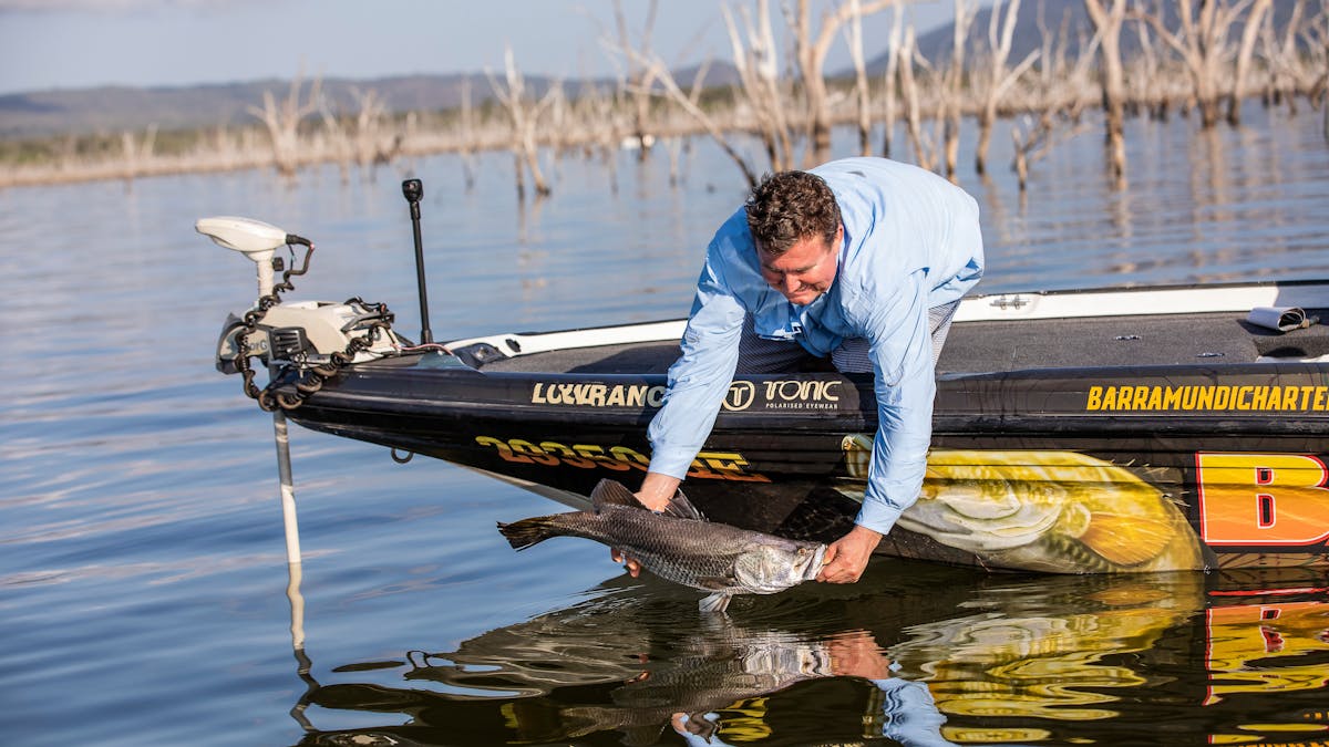 A fisherman taking barramundi out of the water at Lake Proserpine