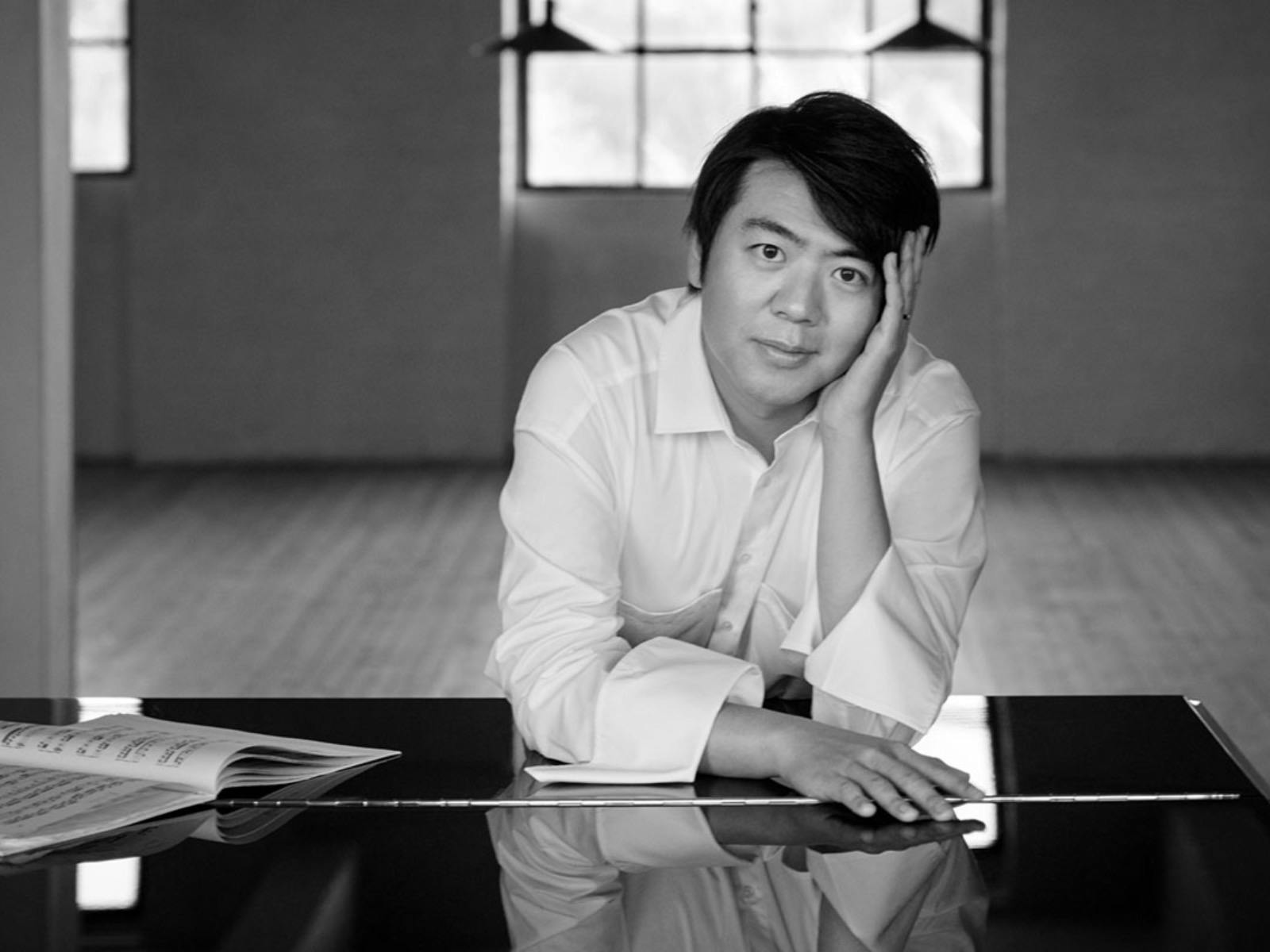 Lang Lang poses, leaning on a piano top in a black and white photo