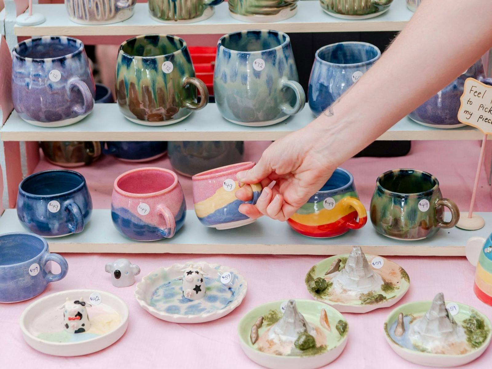 A hand grabbing a mug from a selection of colourful mugs