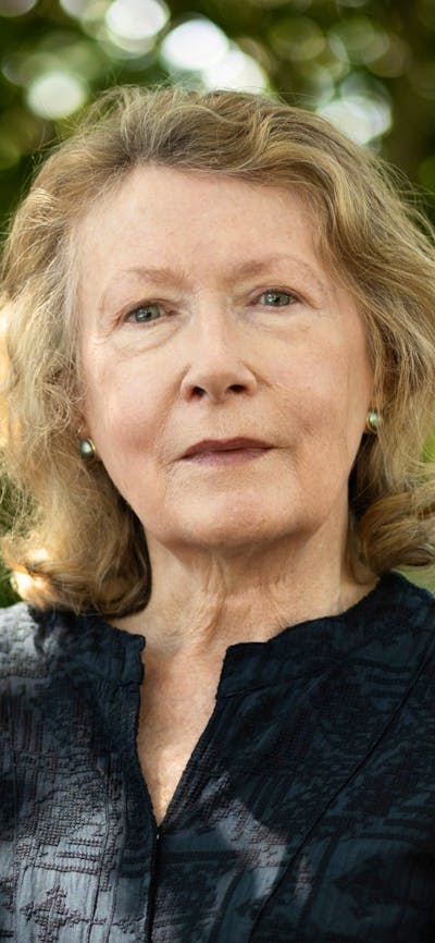 Photo of author A L Booth sitting on a park bench, in a black top with greenery in the background.