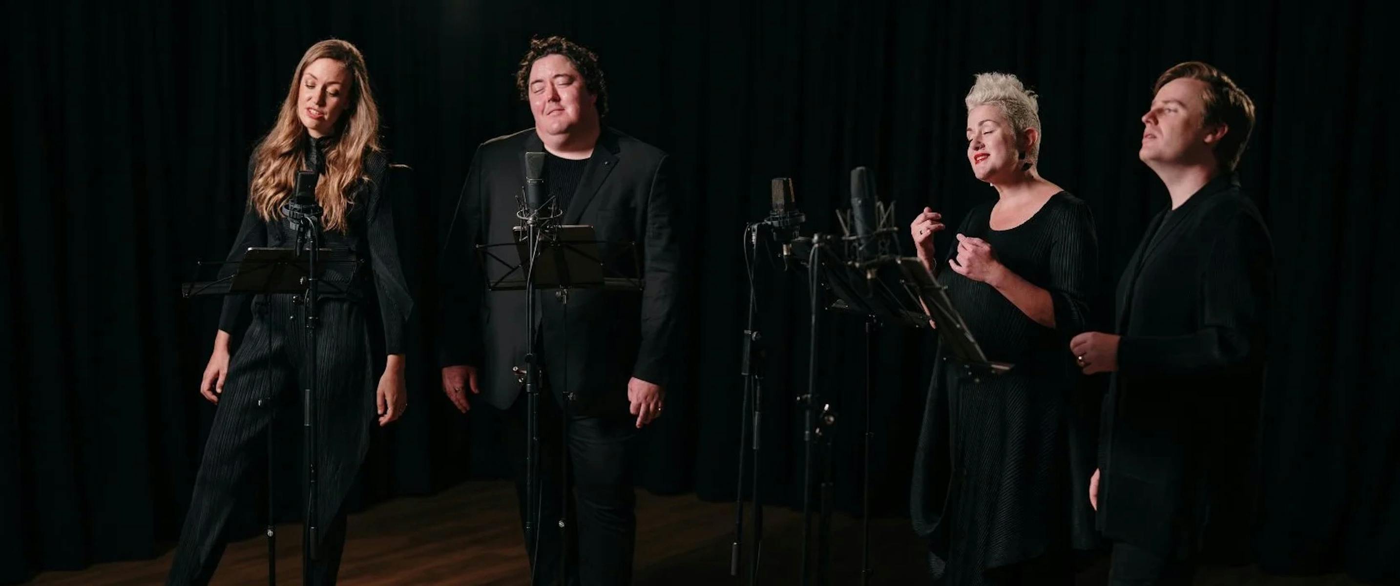 Australian Vocal Ensembe: 4 vocalists wearing black stand in-front of microphones and music stands.