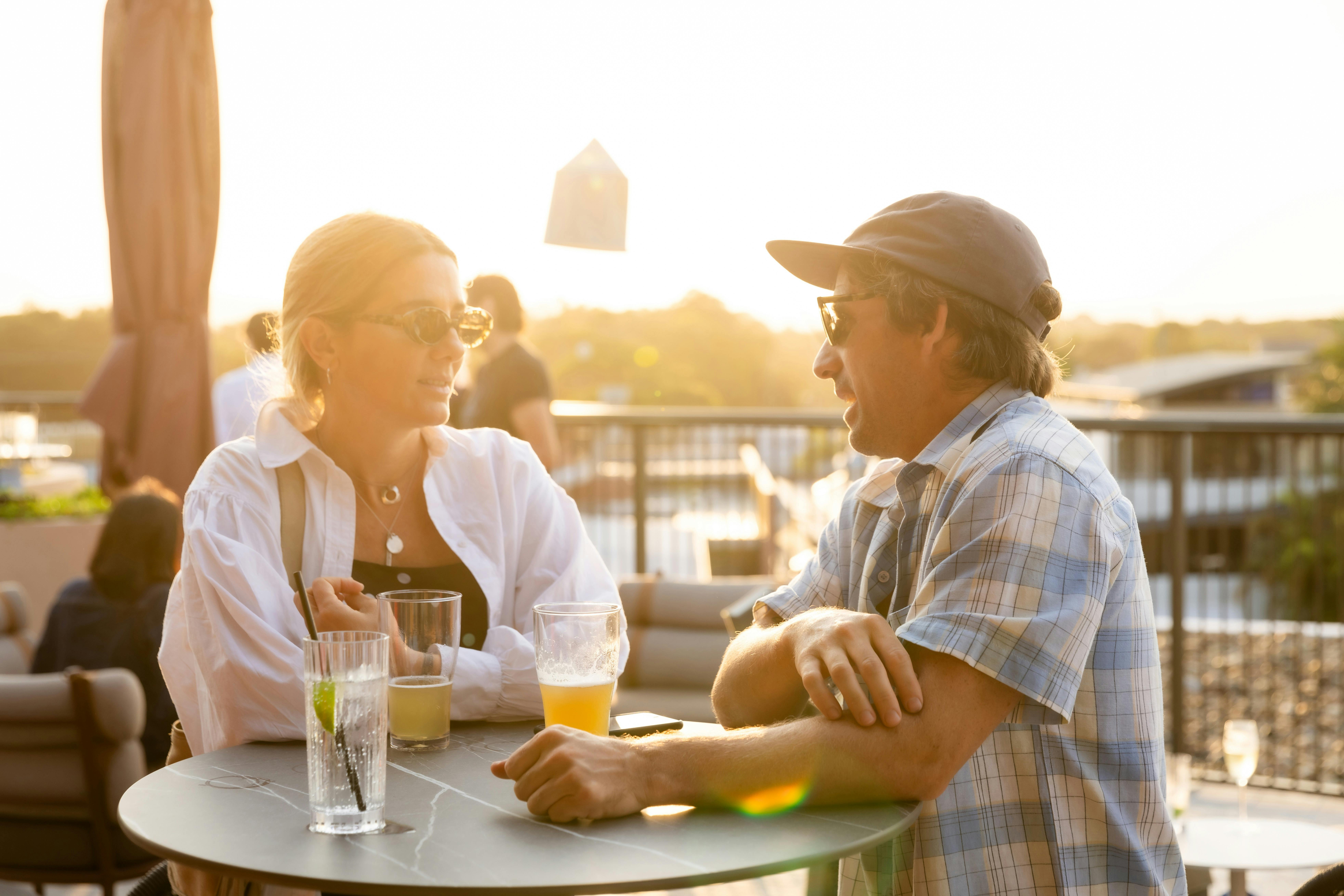 A woman and a man are bathed in sunlight as they enjoy a drink on the Hotel Marvell Rooftop Bar
