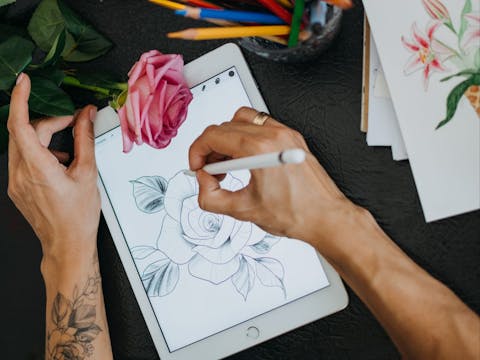 Woman's hands sketching an illustration of a rose on an iPad with a digital stylus