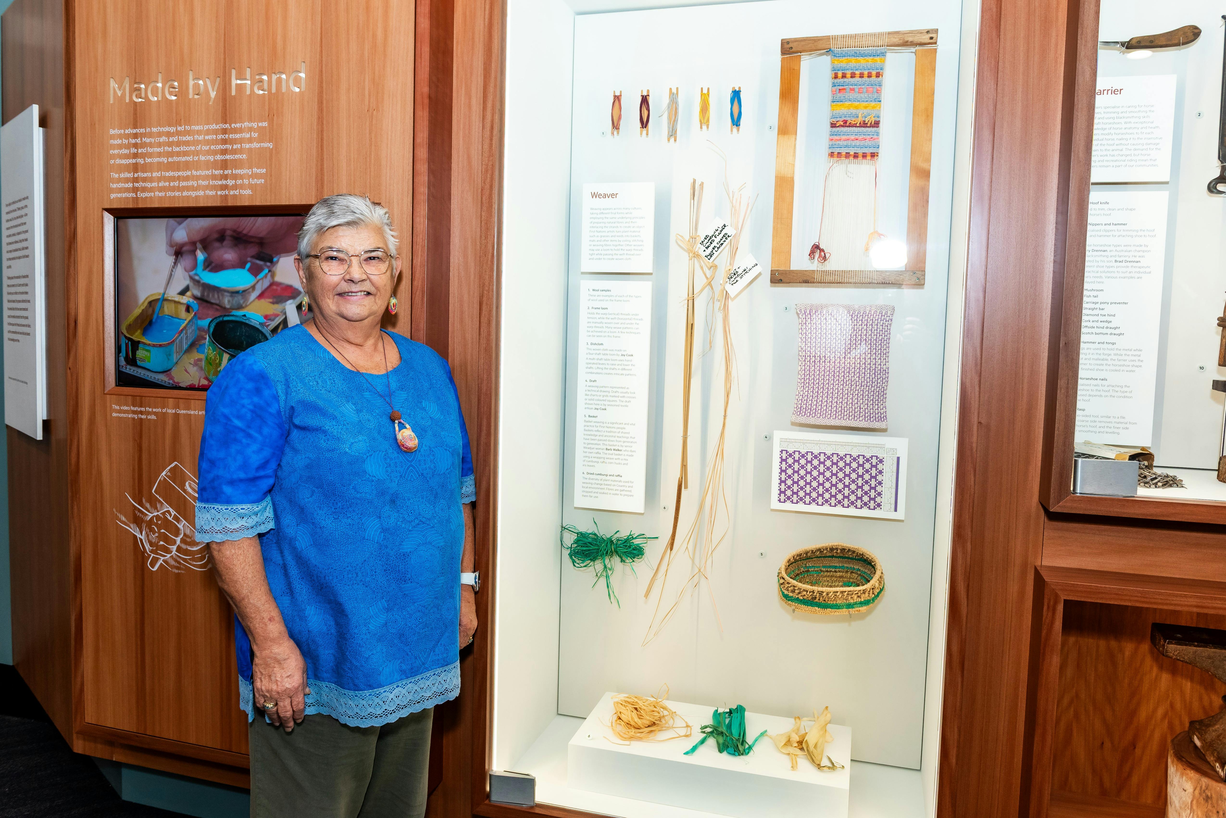 Aunty Barb standing beside gallery display of her woven basket and materials