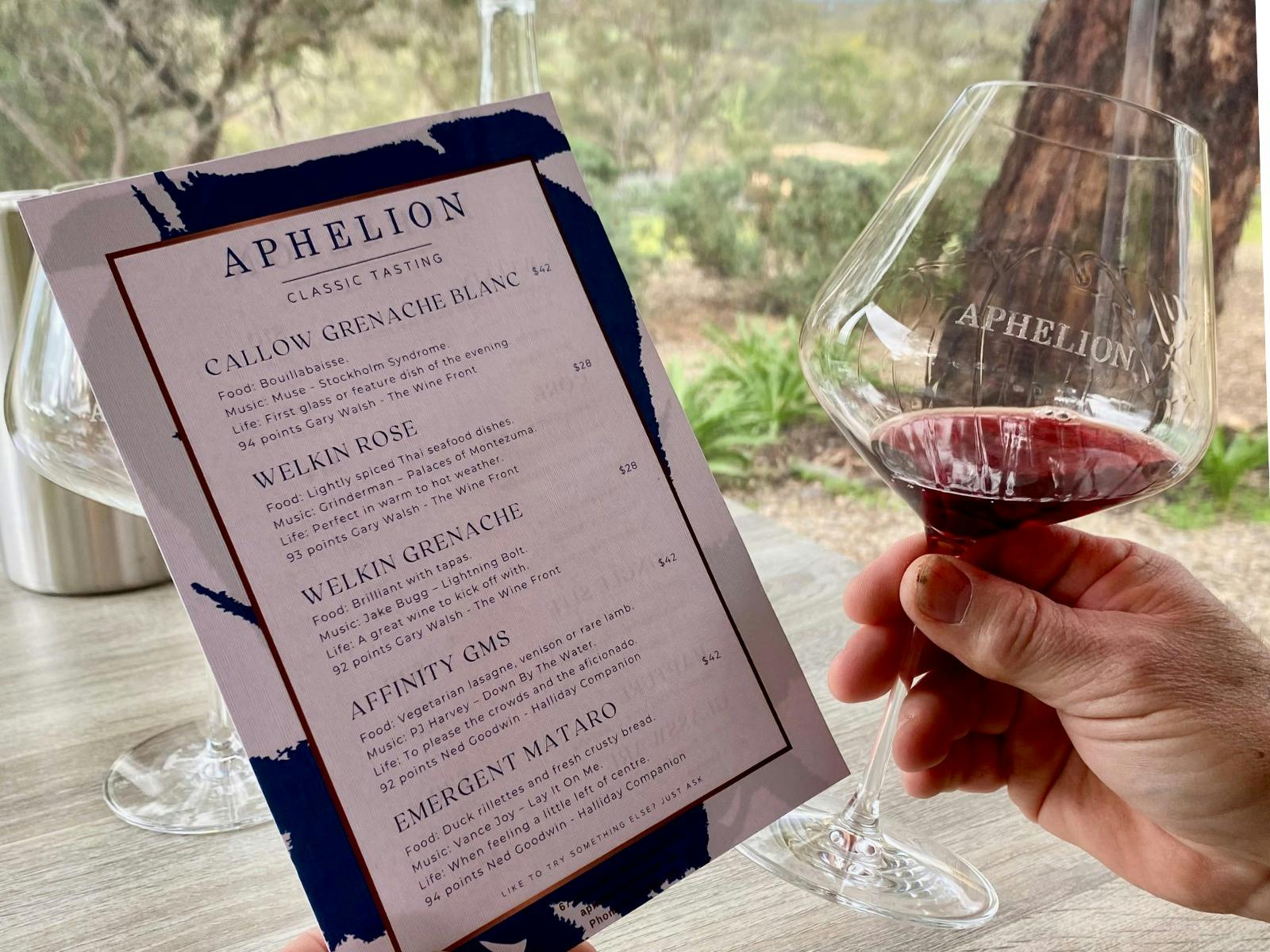 A card listing the wines of an Aphelion Reserve Cellar Door Tasting and a glass of Grenache