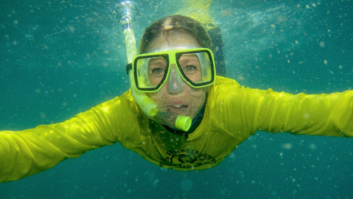 person snorkelling underwater wearing yellow swim shirt and smiling and having fun snorkelling
