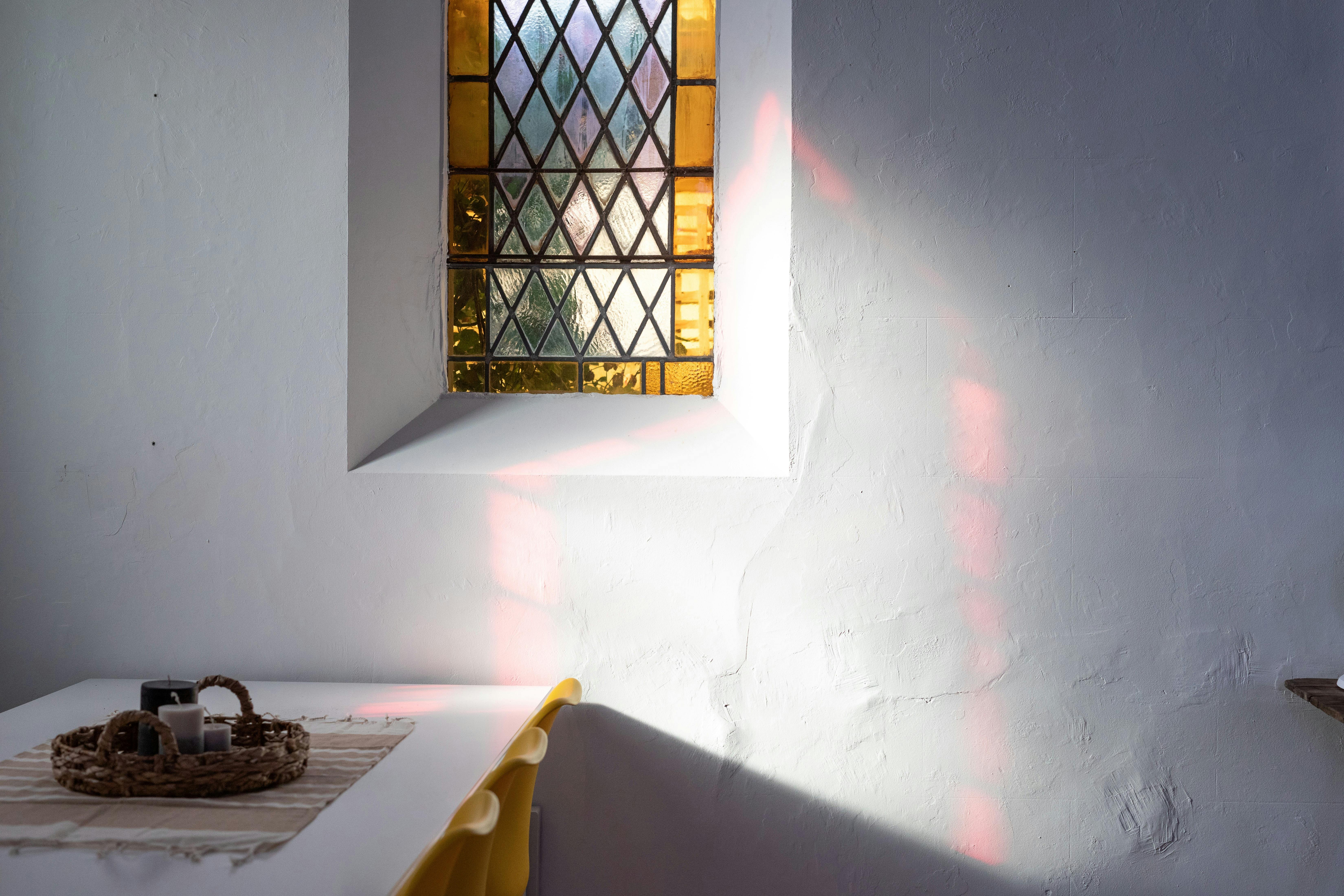 Dining table with a yellow stained glass window above and reflected red light from another window