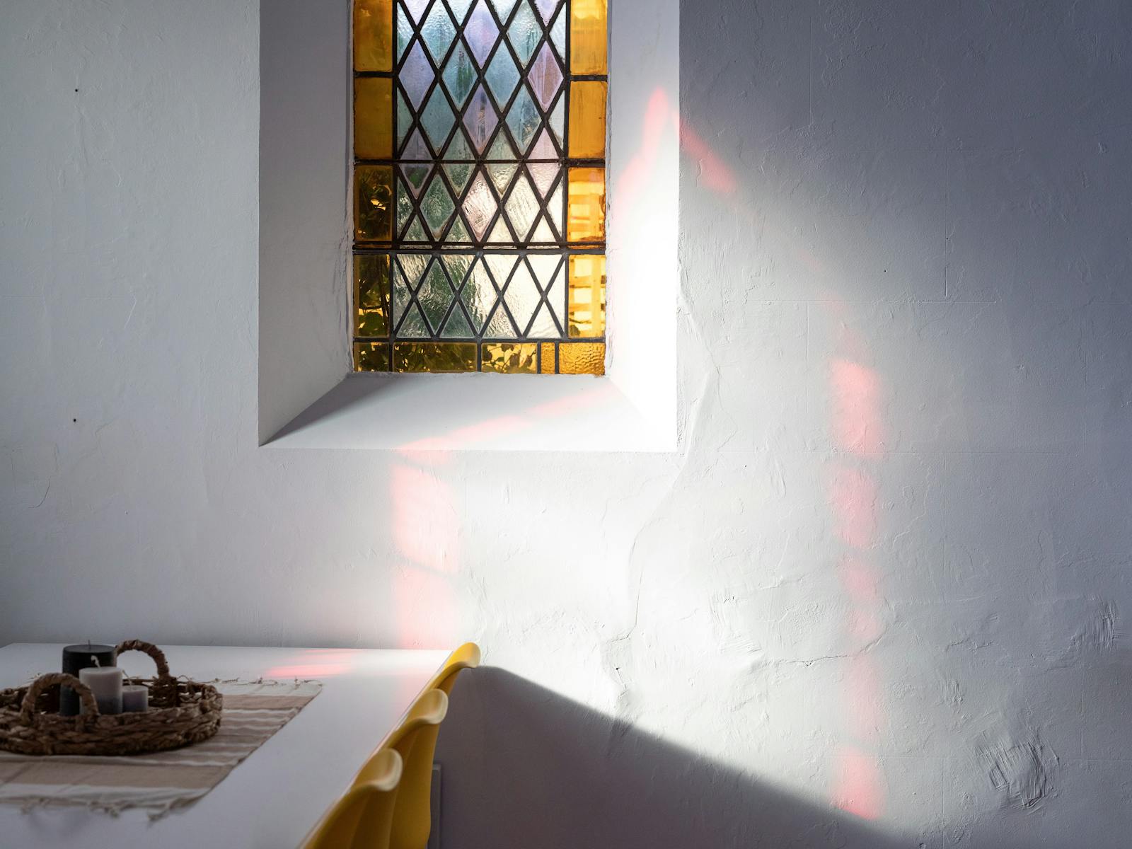Dining table with a yellow stained glass window above and reflected red light from another window