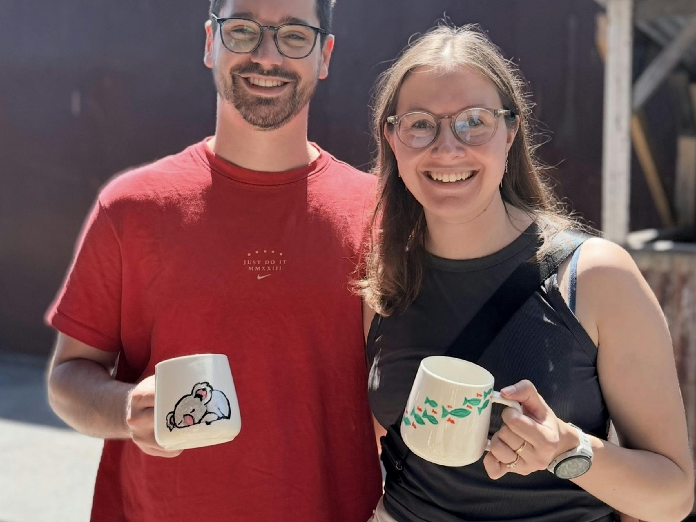 Two guests holding the ceramic mugs they painted at the workshop