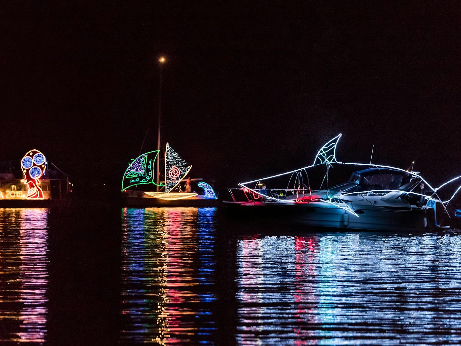 Boats on lake at night time lit up with colourful fairy lights