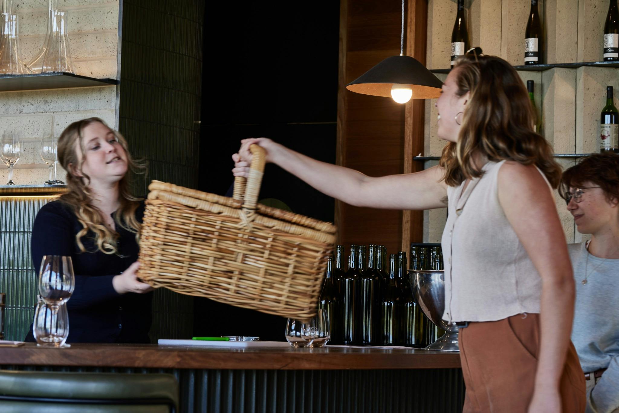 A person standing behind a bar, handing over a picnic basket