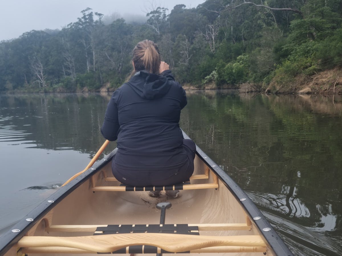 The back of a woman sat in a canoe, canoeing down the river