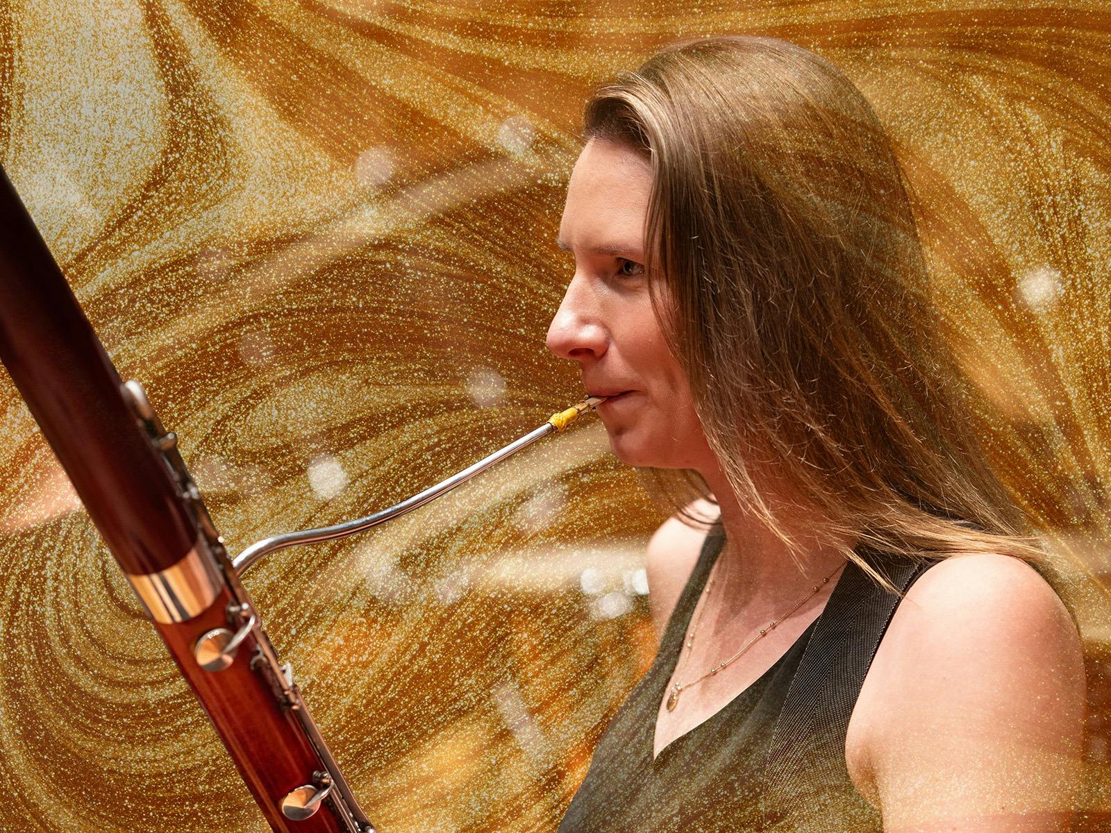 A female meusician with long blonde hair plays the oboe, there are gold shimmery layers over laid