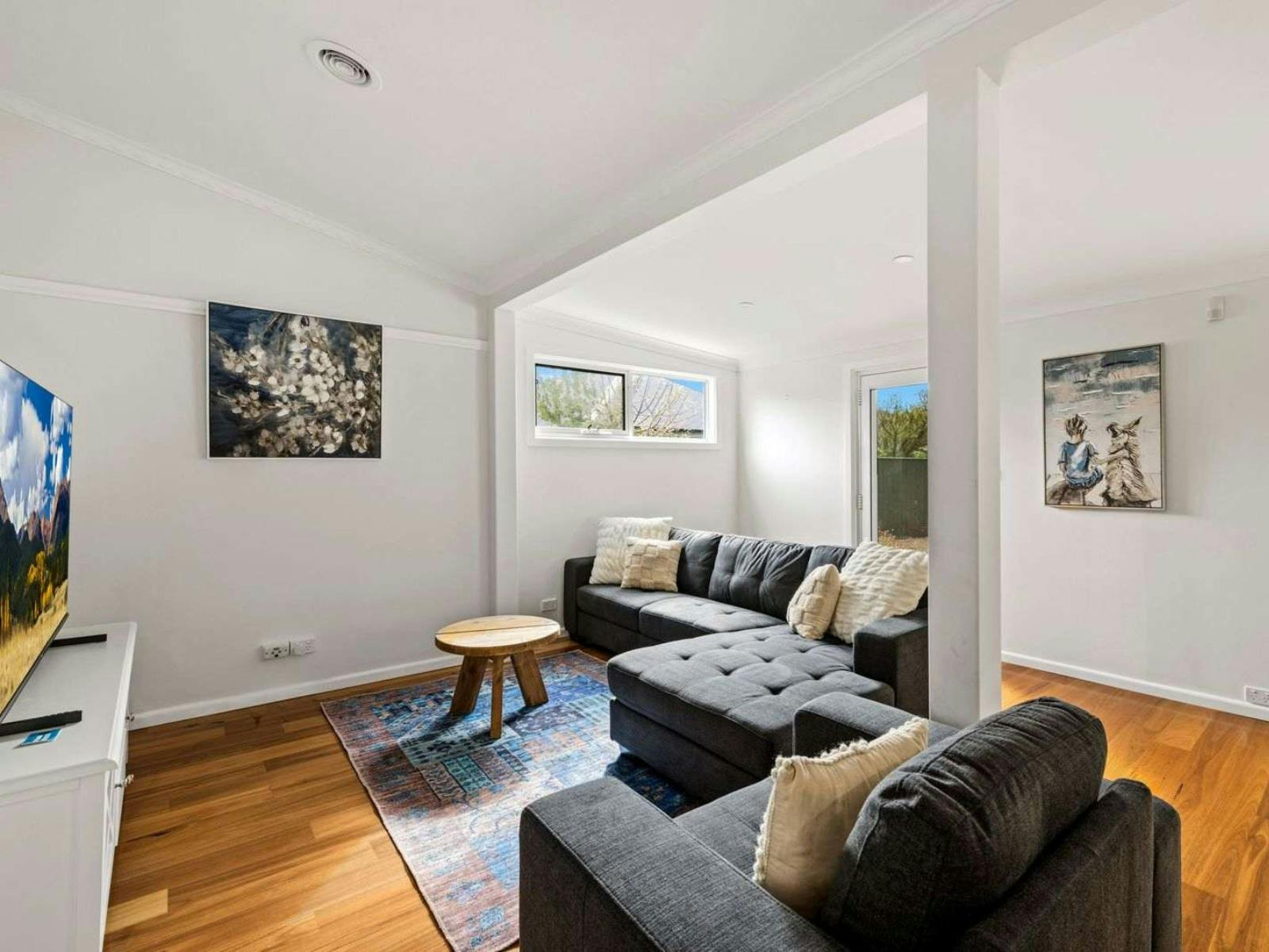 Living room with 2 couches, smart tv, rug, white walls and art on wall