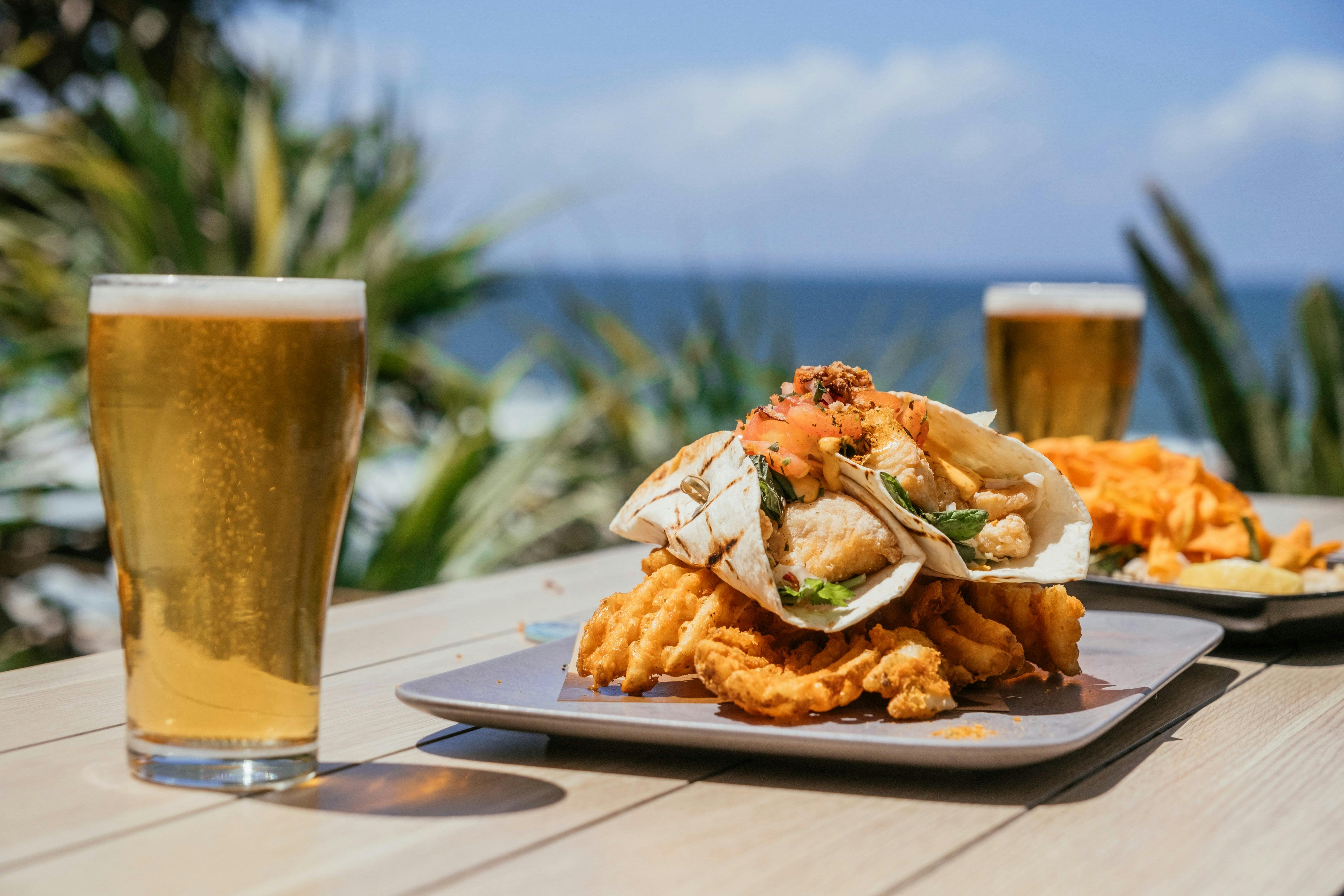 Two schooners of beer and a plate containing a wrap and chips