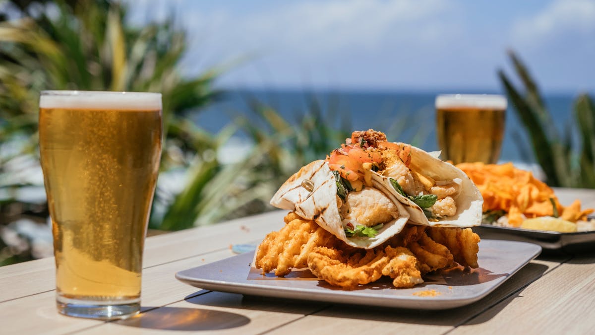 Two schooners of beer and a plate containing a wrap and chips