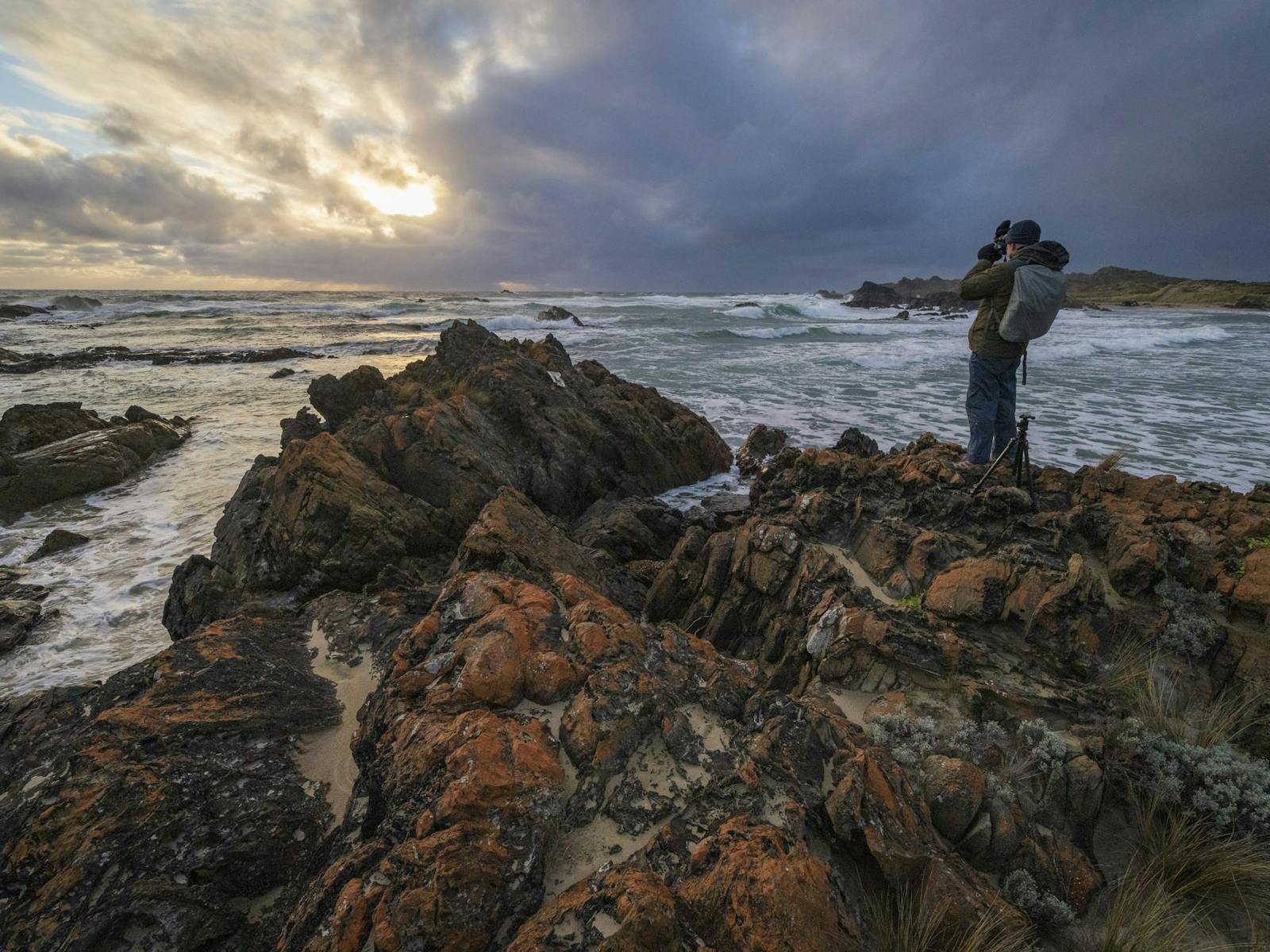 A photographer stands on the wild and remote Tarkine coast at sunset