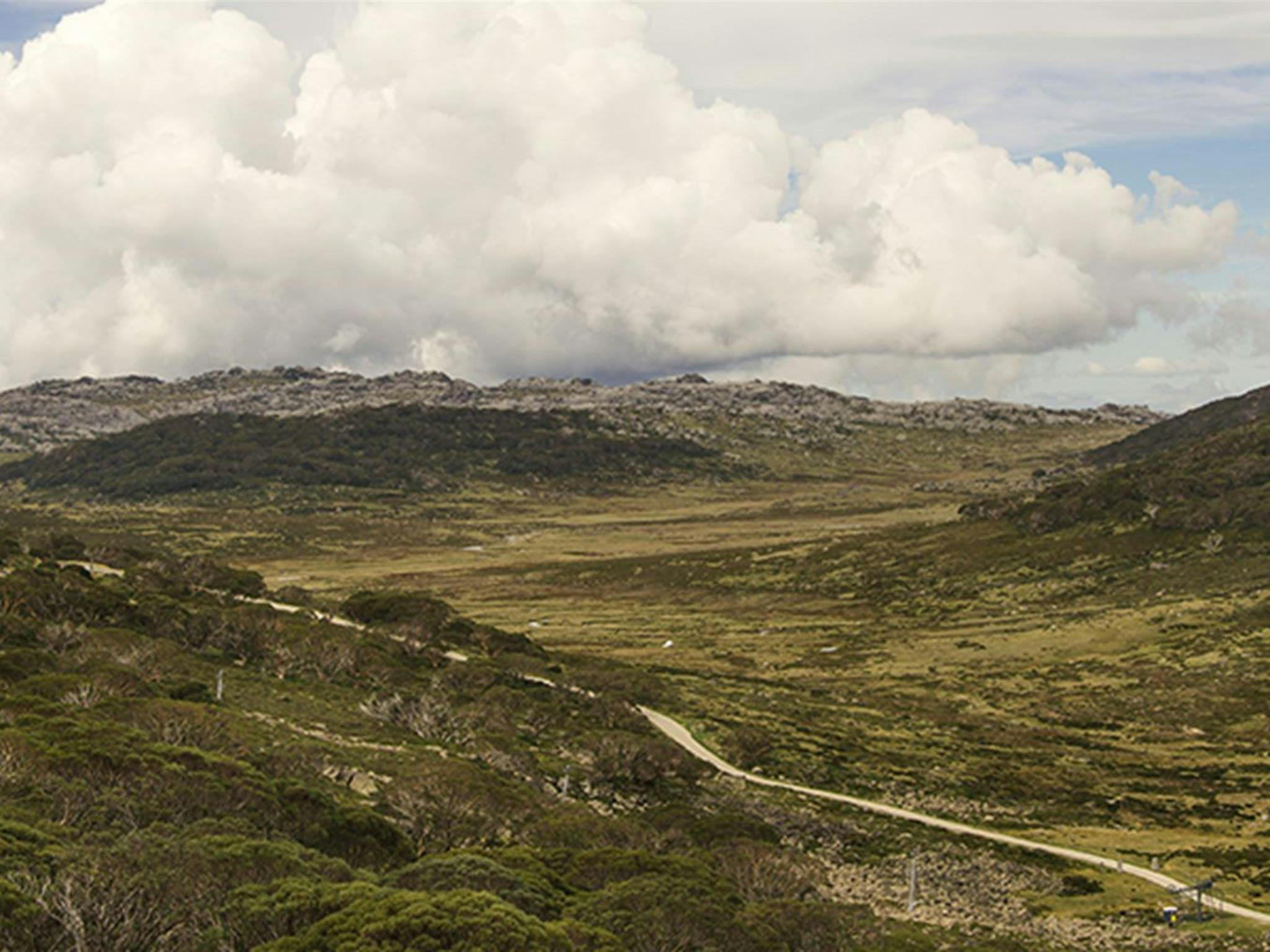 部分的に曇り空の下で、ダートトラックが横断する開放的で険しい山の風景の広い視野。
