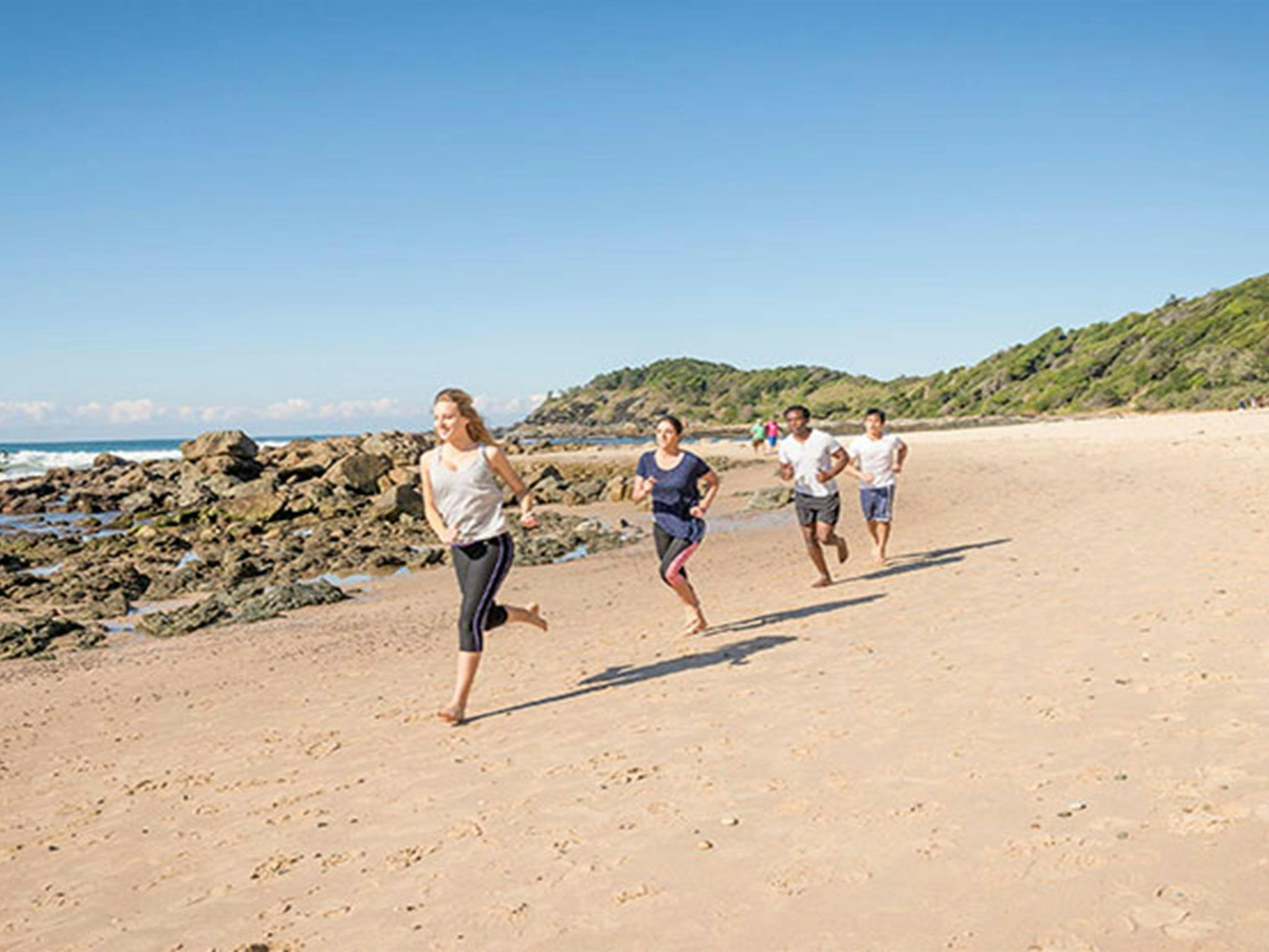 Eine Gruppe von Menschen, die am Strand entlang des Küstenwanderwegs von Port Macquarie in Sea Acres Sport treiben.