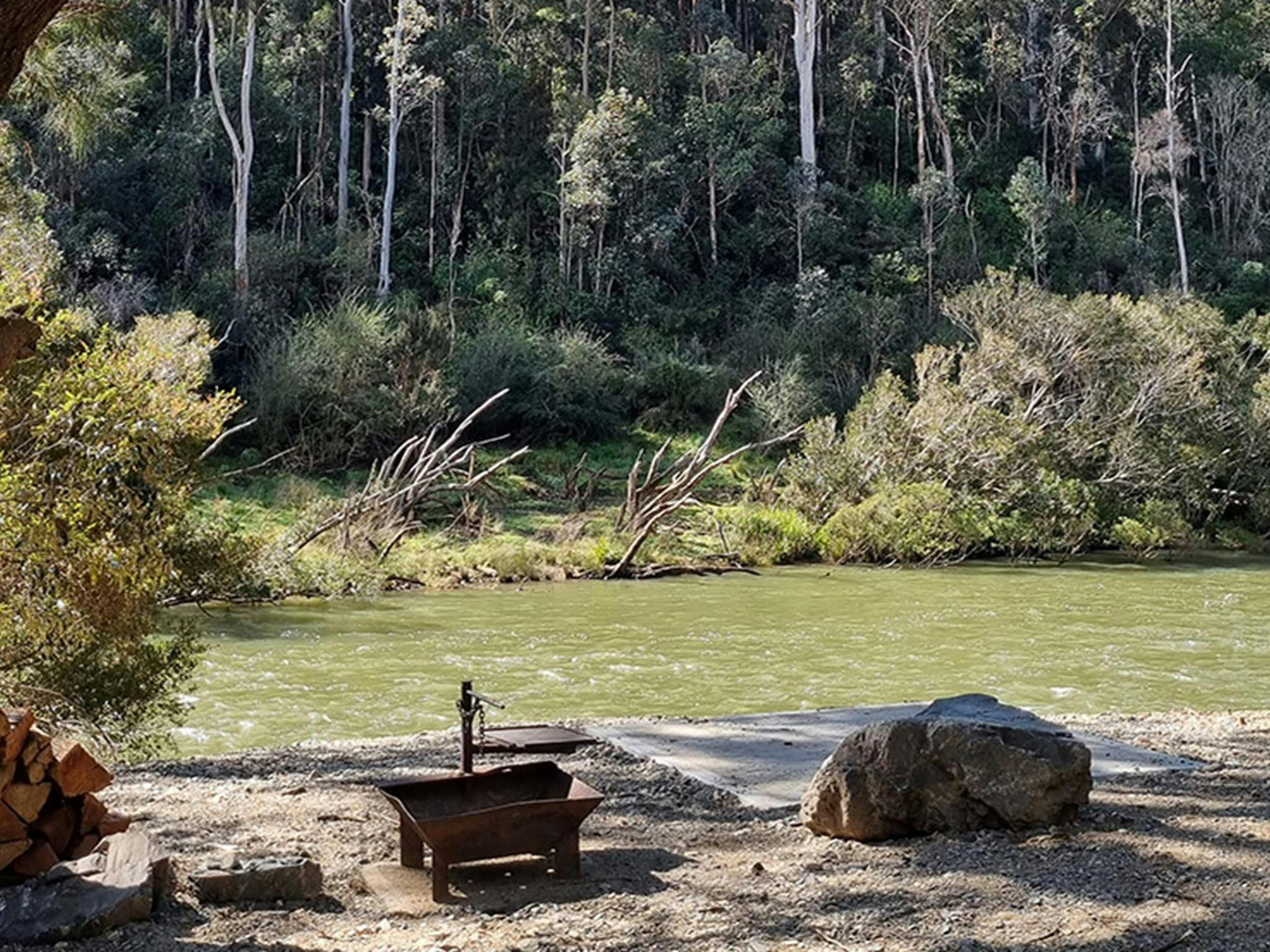 A campsite with a wood barbecue near the shore of the Nymboida River at Cod Hole campground and
