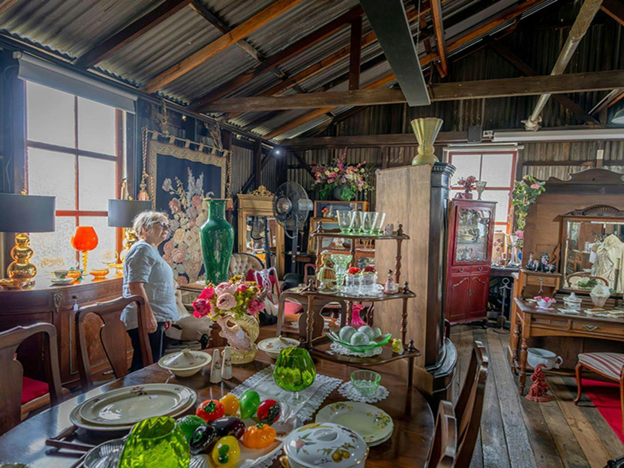 Gold Rush Antiques에서 판매되는 골동품으로 둘러싸인 앤틱 녹색 꽃병을 보고 있는 방문객