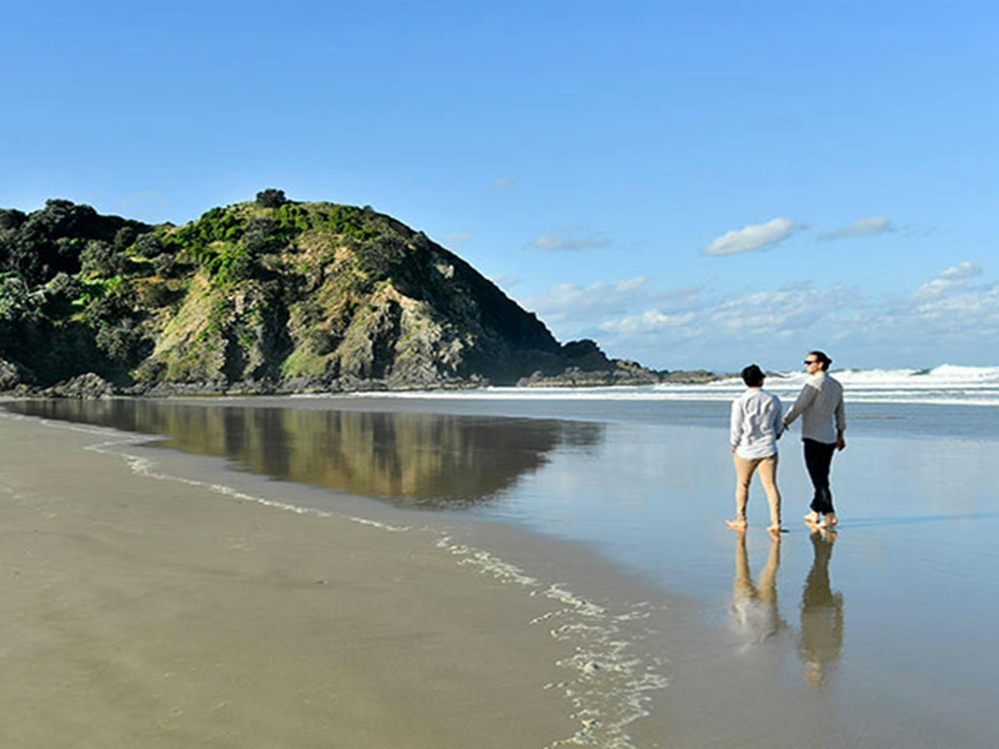 A couple walking along the sand at Tallow Beach in Cape Byron State Conservation Area. Photo: Fiora