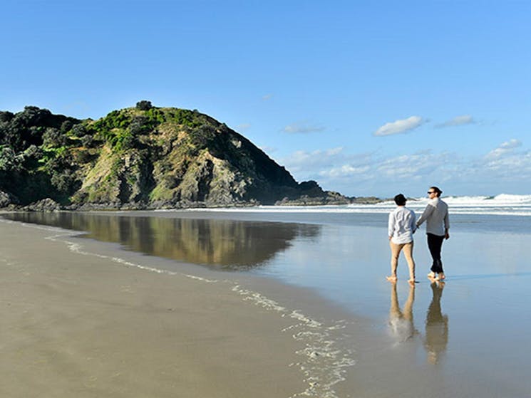 A couple walking along the sand at Tallow Beach in Cape Byron State Conservation Area. Photo: Fiora