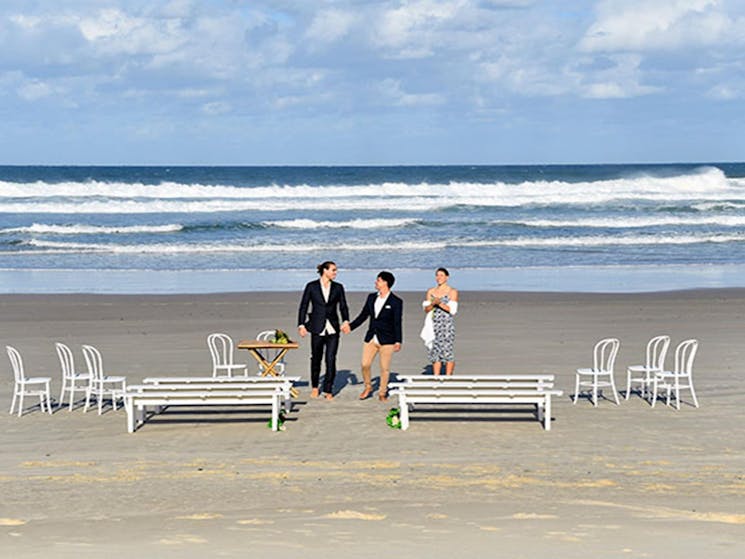A couple and their celebrant with the ocean in the background at Cosy Corner at Tallow Beach. Photo: