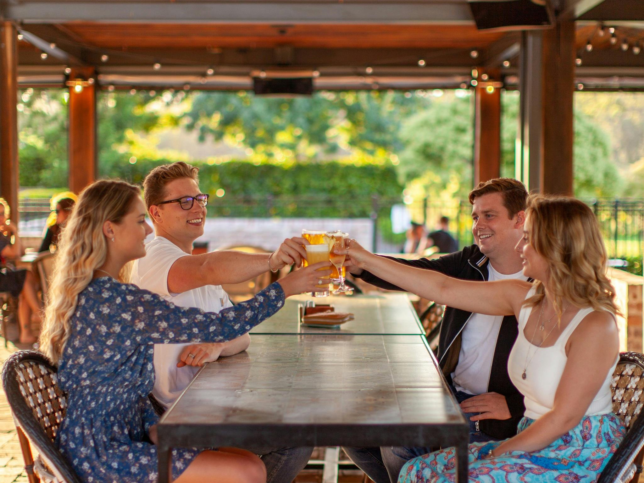 Two women and two men sitting at an outdoor table at Harrigan's Hunter Valley cheersing their drinks