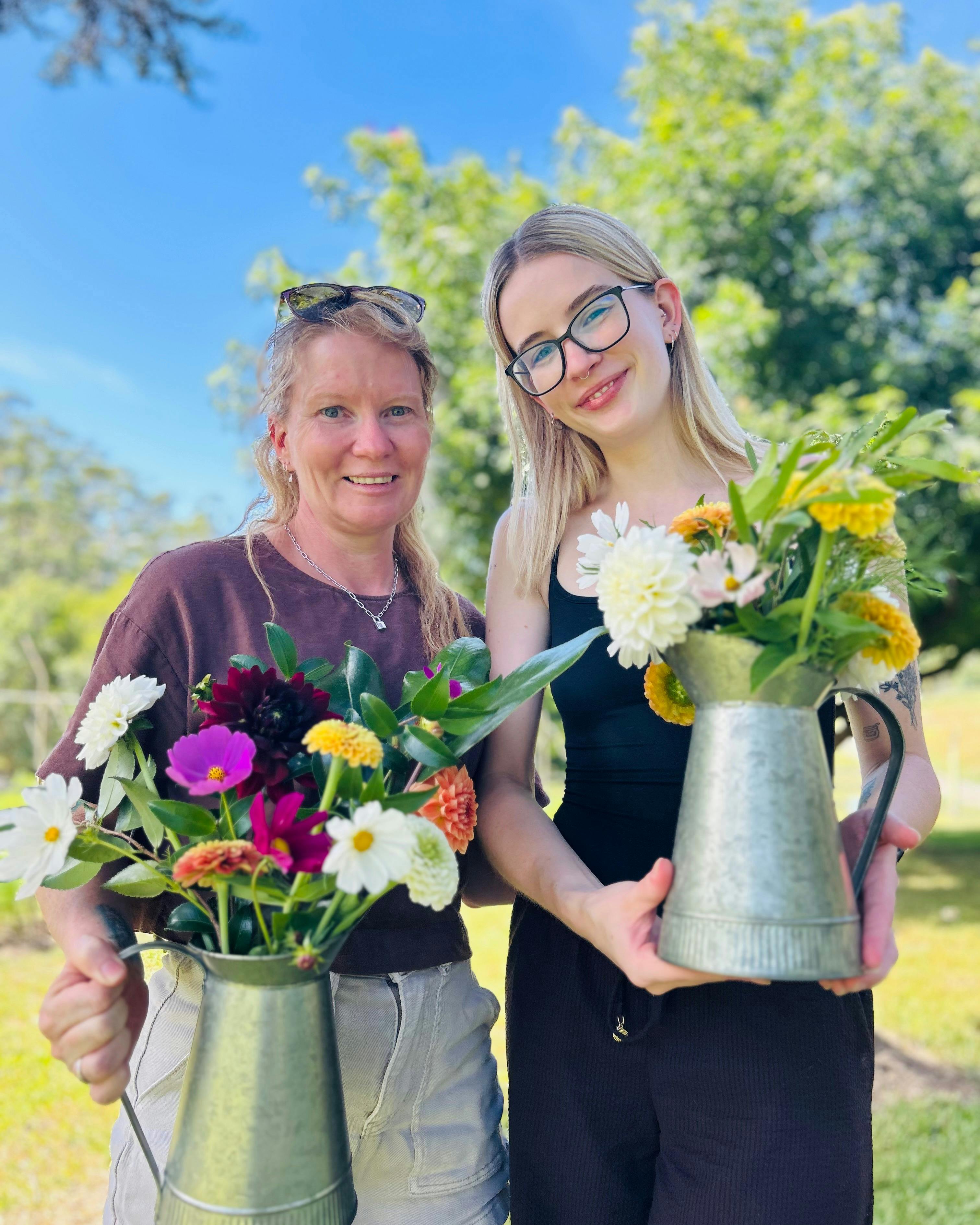 Two women holding metal vases with flowers
