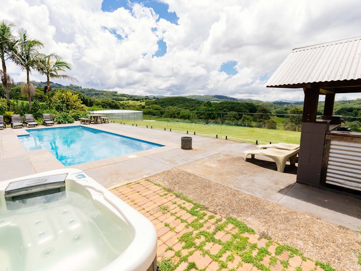 A hot tub, pool and a gazebo on a sunny day overlooking the Byron Bay hinterland and valley