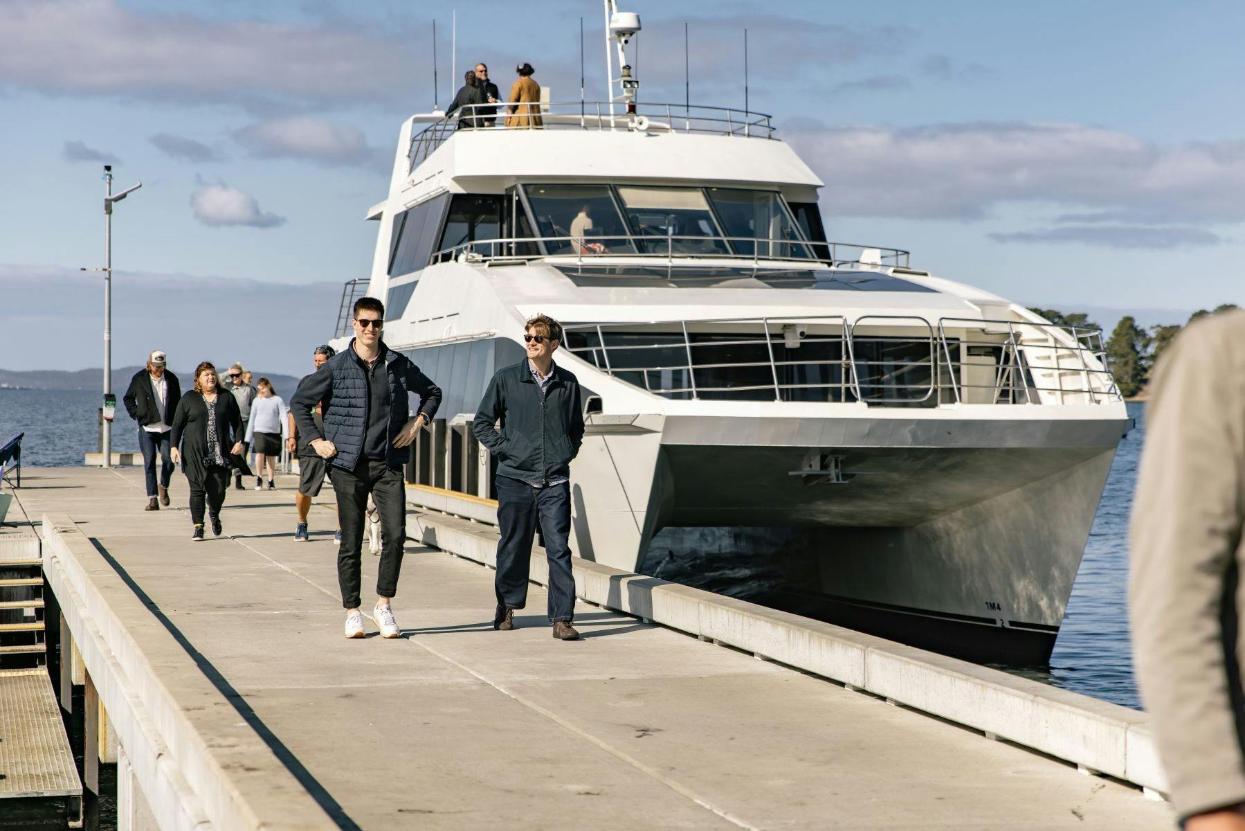 Two young men disembarking a catamaran and walking along a jetty