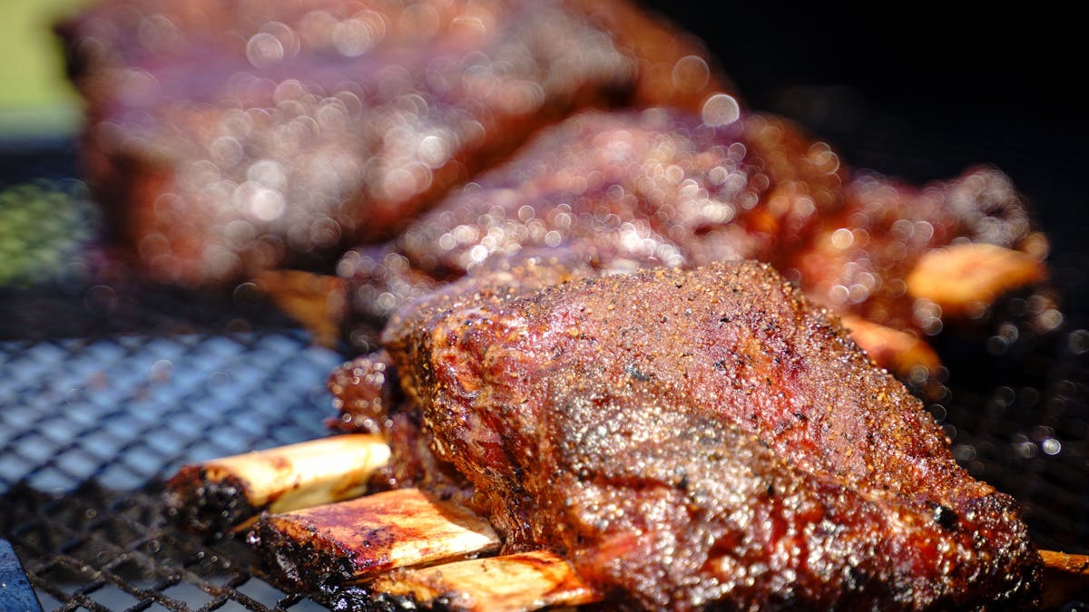 Authentic Low and Slow BBQ Ribs at Meat Noosa – Glazed, smoky ribs sizzling on the grill, ready to b