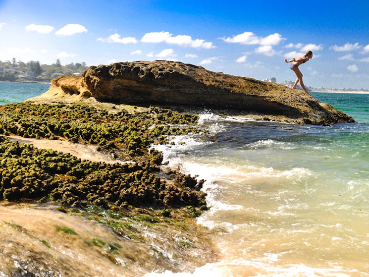 Girl diving into ocean waters from rocks