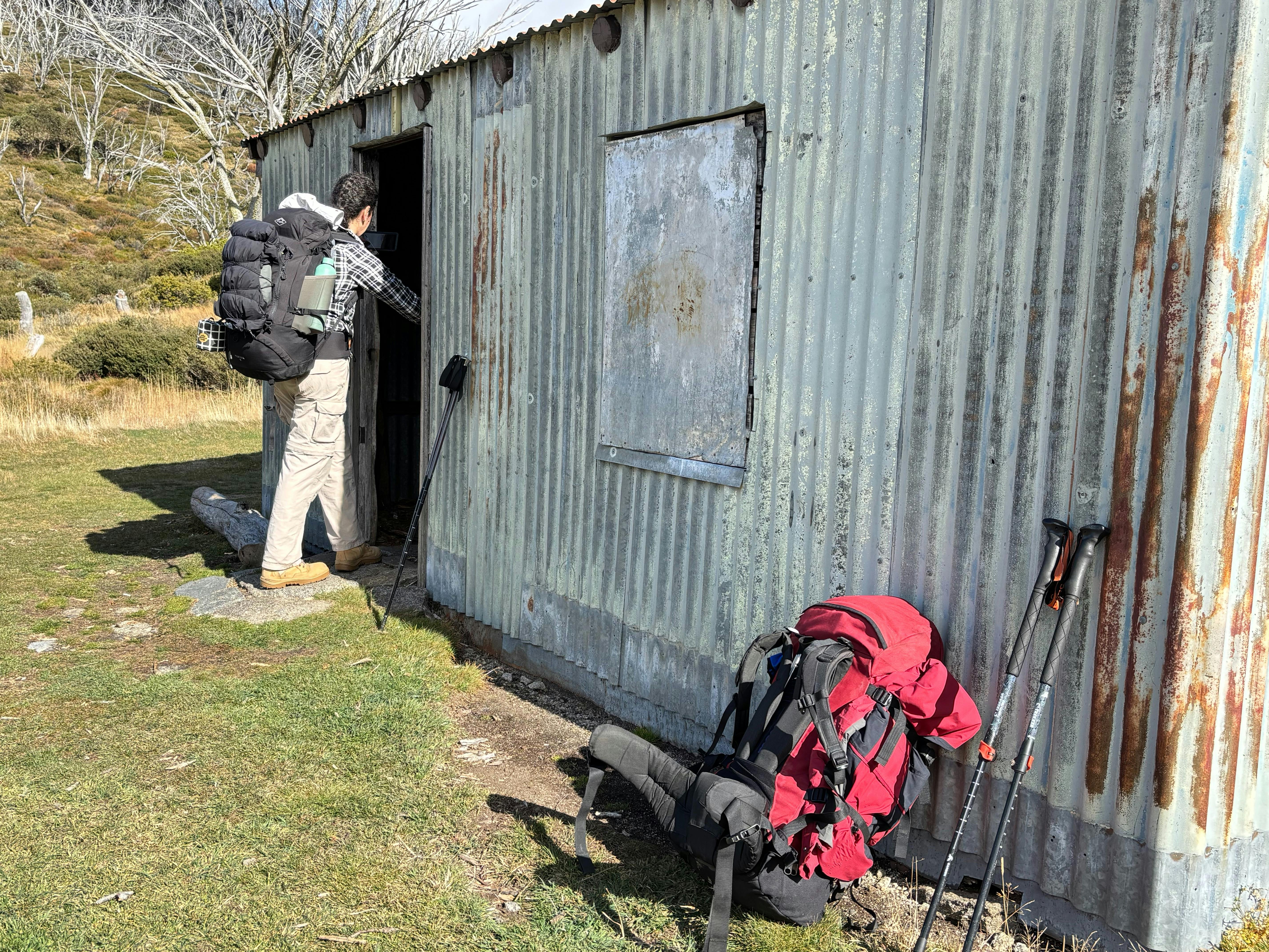 Woman wearing white jeans and checked shirt entering the door of a corrugated iron hut