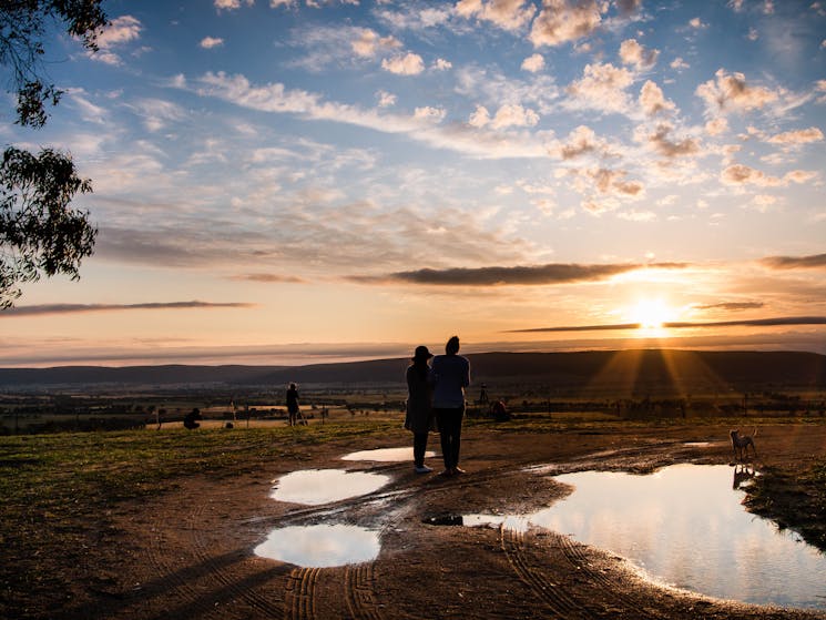 Two people viewing the sunrise over the countryside from elevated hillside