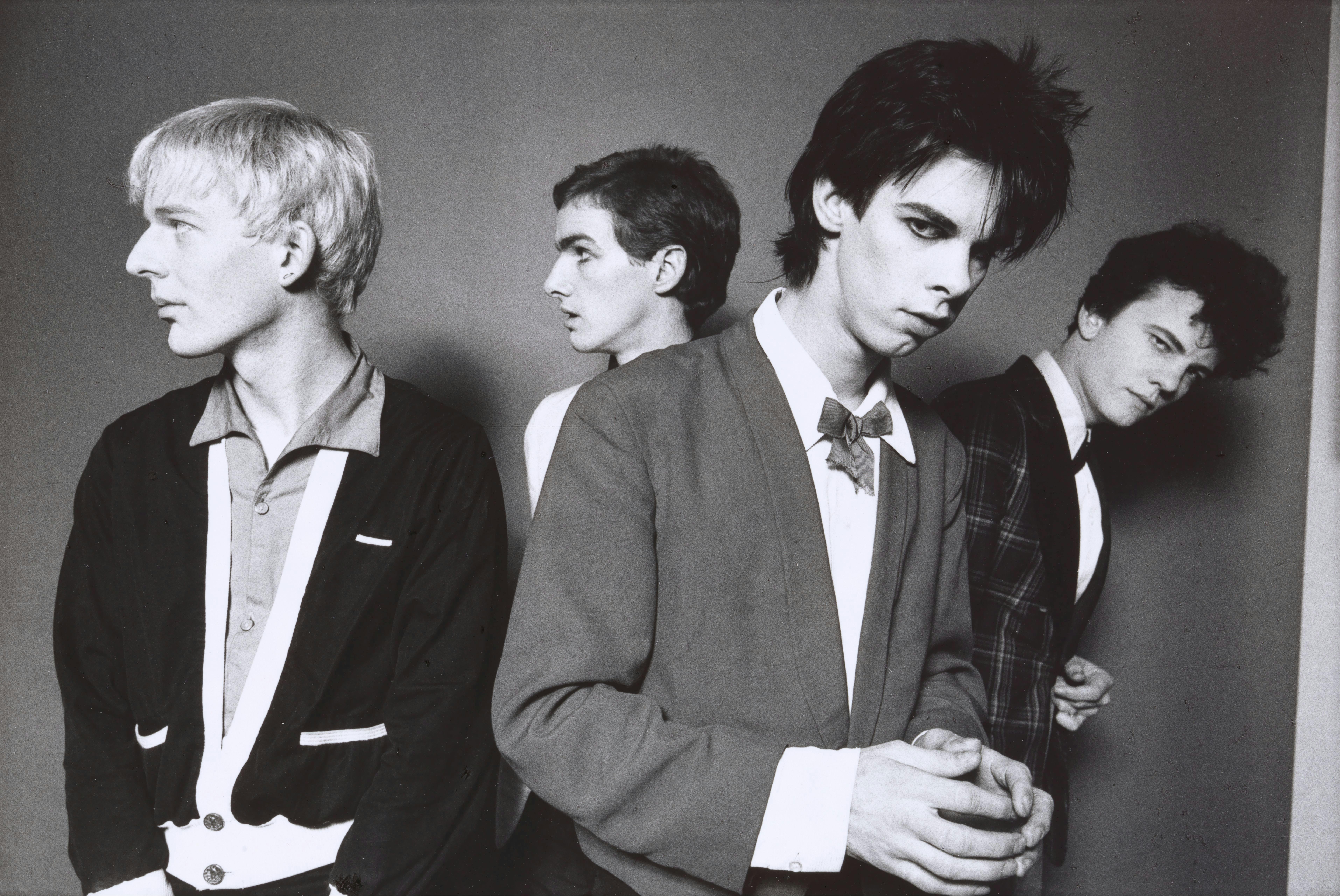 A monochrome photographic portrait of four men with candid expressions wearing suits.