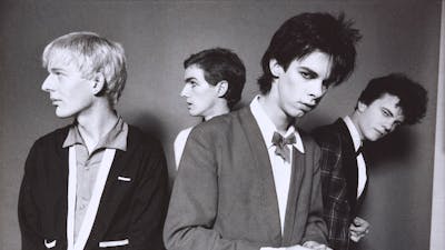 A monochrome photographic portrait of four men with candid expressions wearing suits.