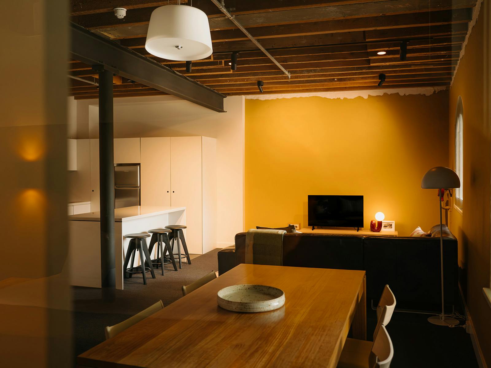Open-plan living area with wood dining table, kitchen island, and exposed timber beams.