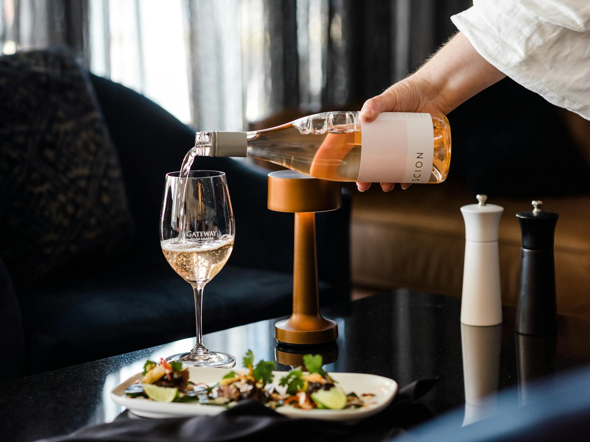 Waiter pouring glass of rose wine to accompany an entree in a moody lounge area at the Gateway