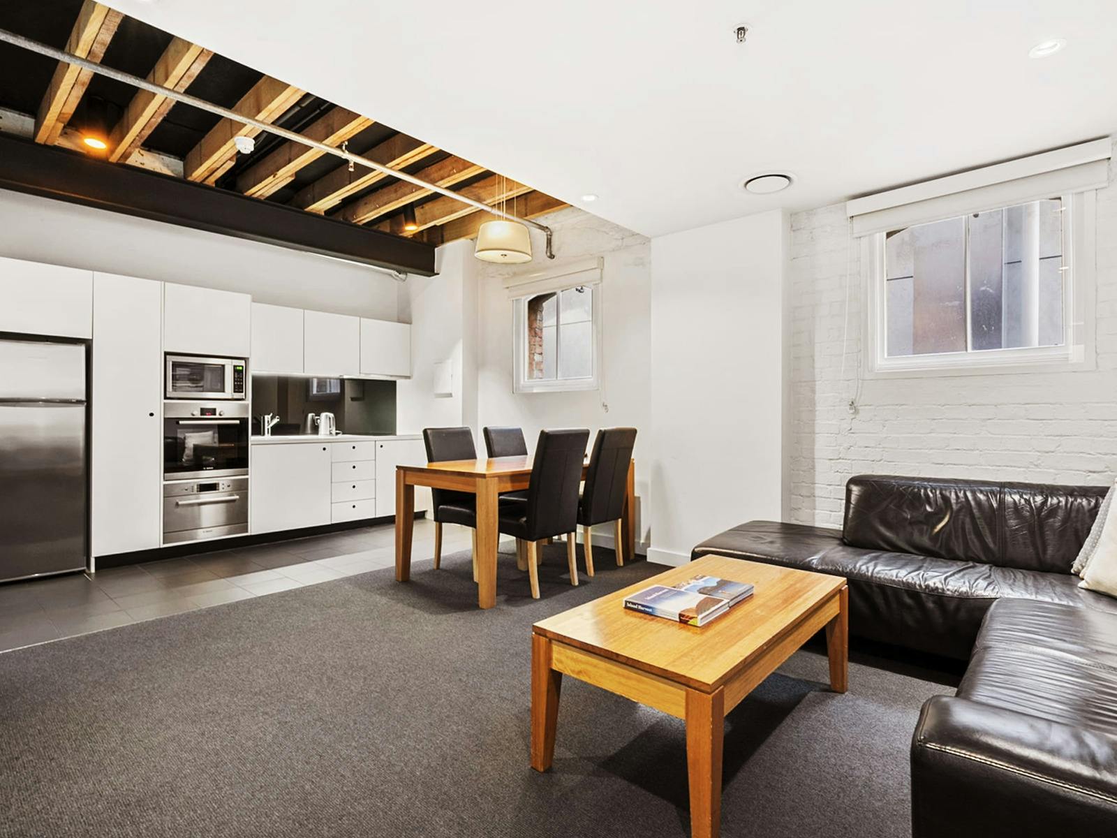 White kitchen and lounge with leather sofas under exposed timber ceiling beams.