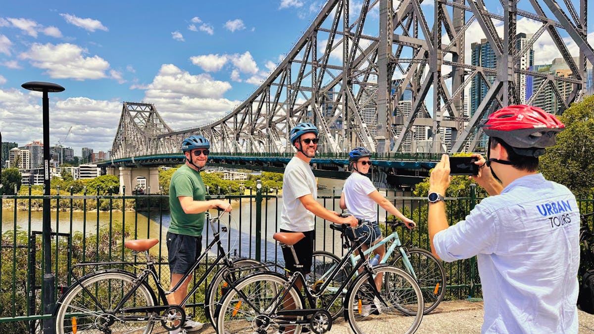 Group of 3 people standing near their pedal bikes with a bridge in the background.