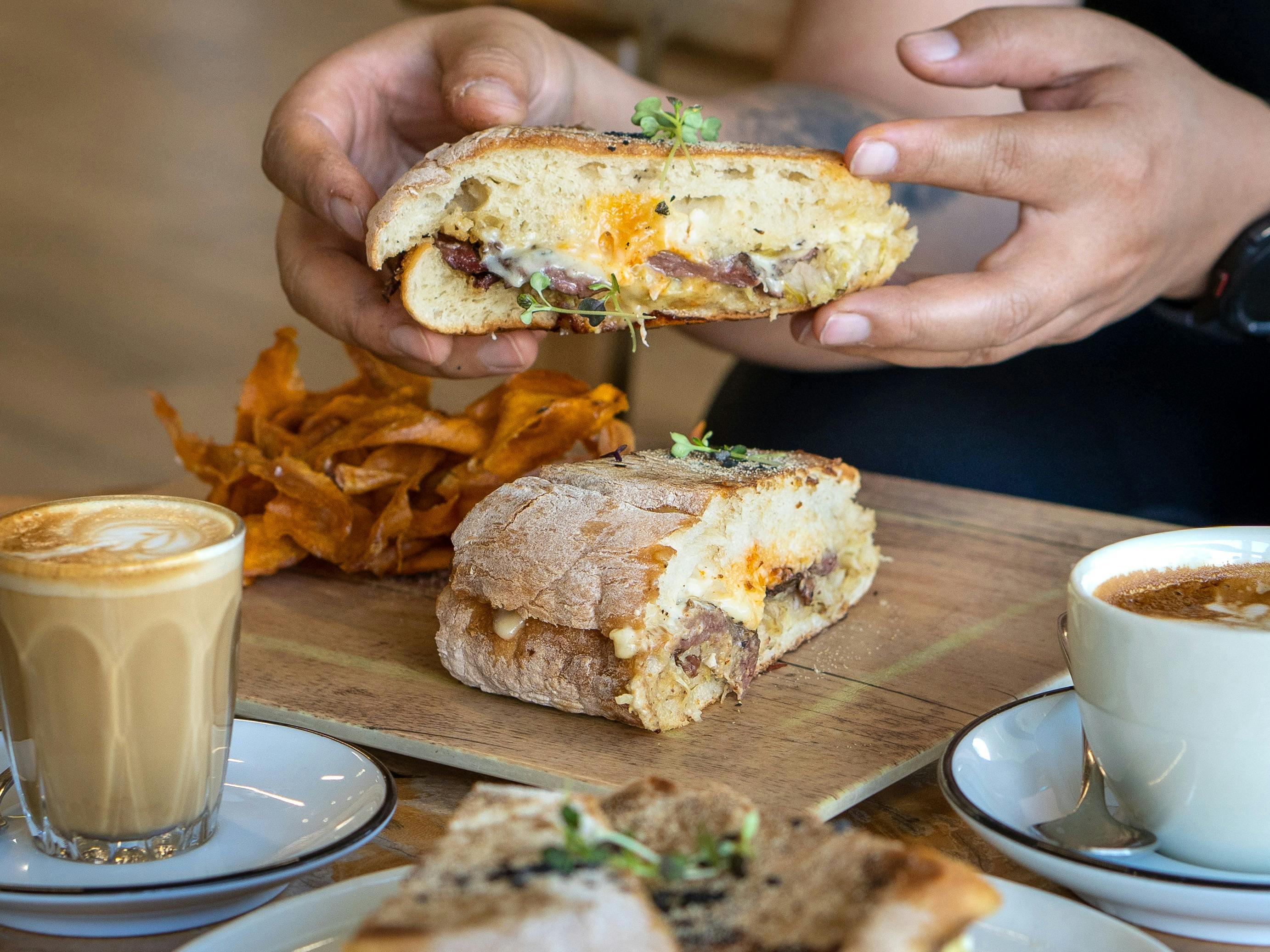A hand holds up half of the sandwich to show the meat and cheese inside